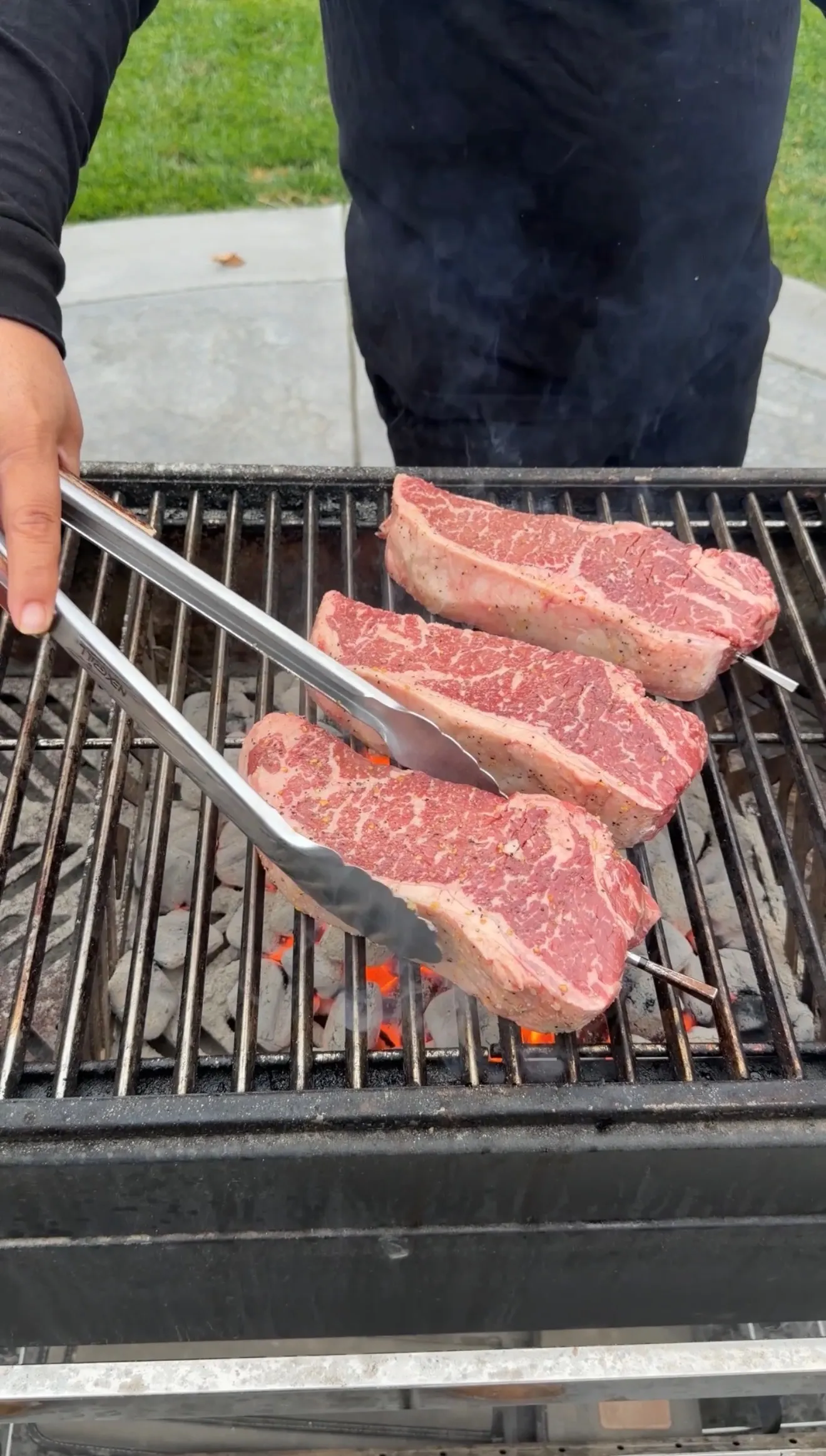 Grilling strip steaks on charcoal grill with tongs