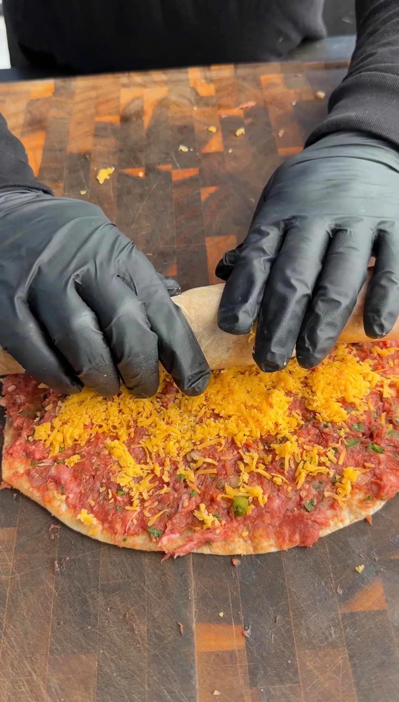 Hands in black gloves preparing grilled lamb tortilla pinwheel with cheese and herbs on cutting board