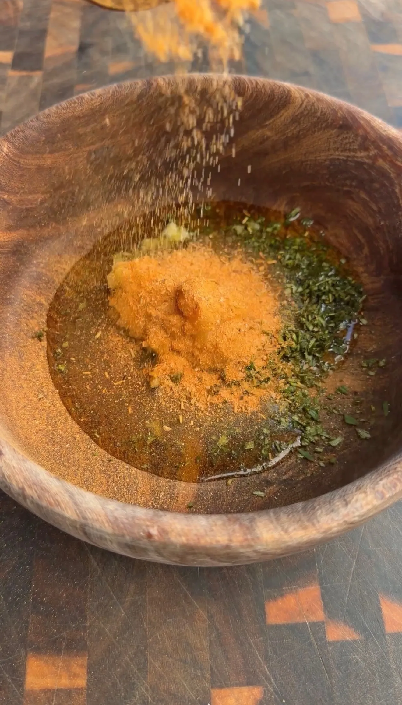Fresh herbs and orange spices being mixed in a rustic wooden bowl for lamb marinade preparation