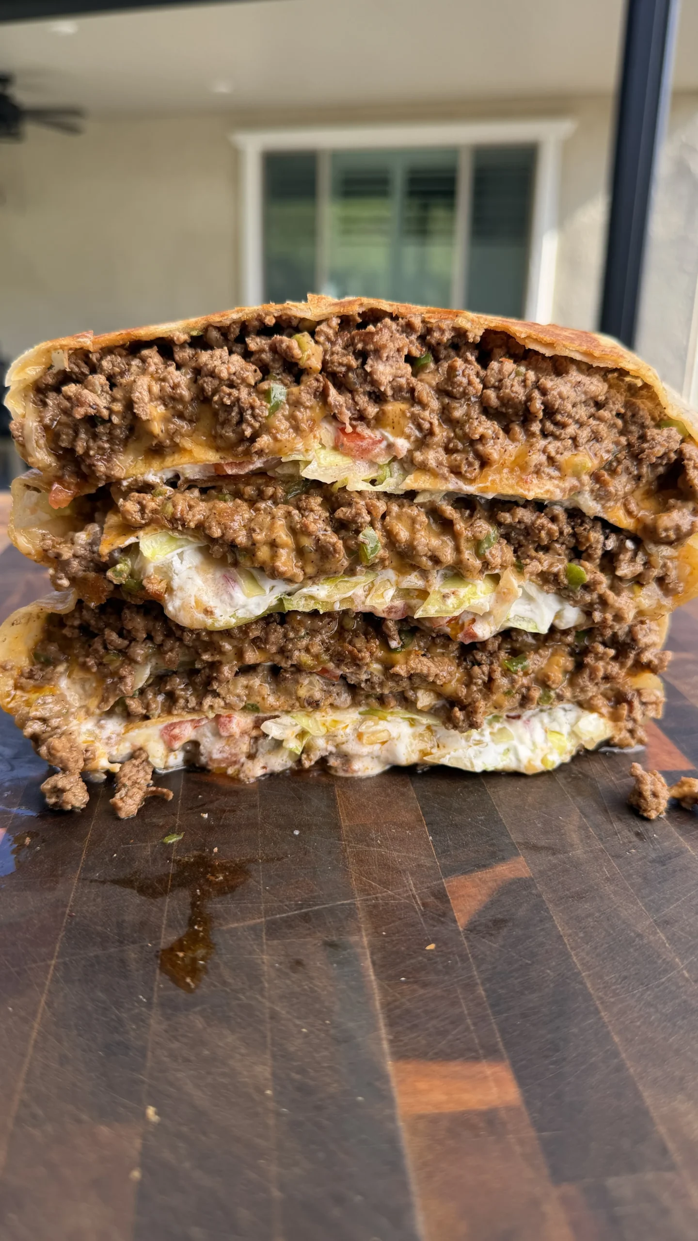 Cross-section of a homemade crunchwrap showing seasoned ground beef, lettuce, and cheese filling on cutting board