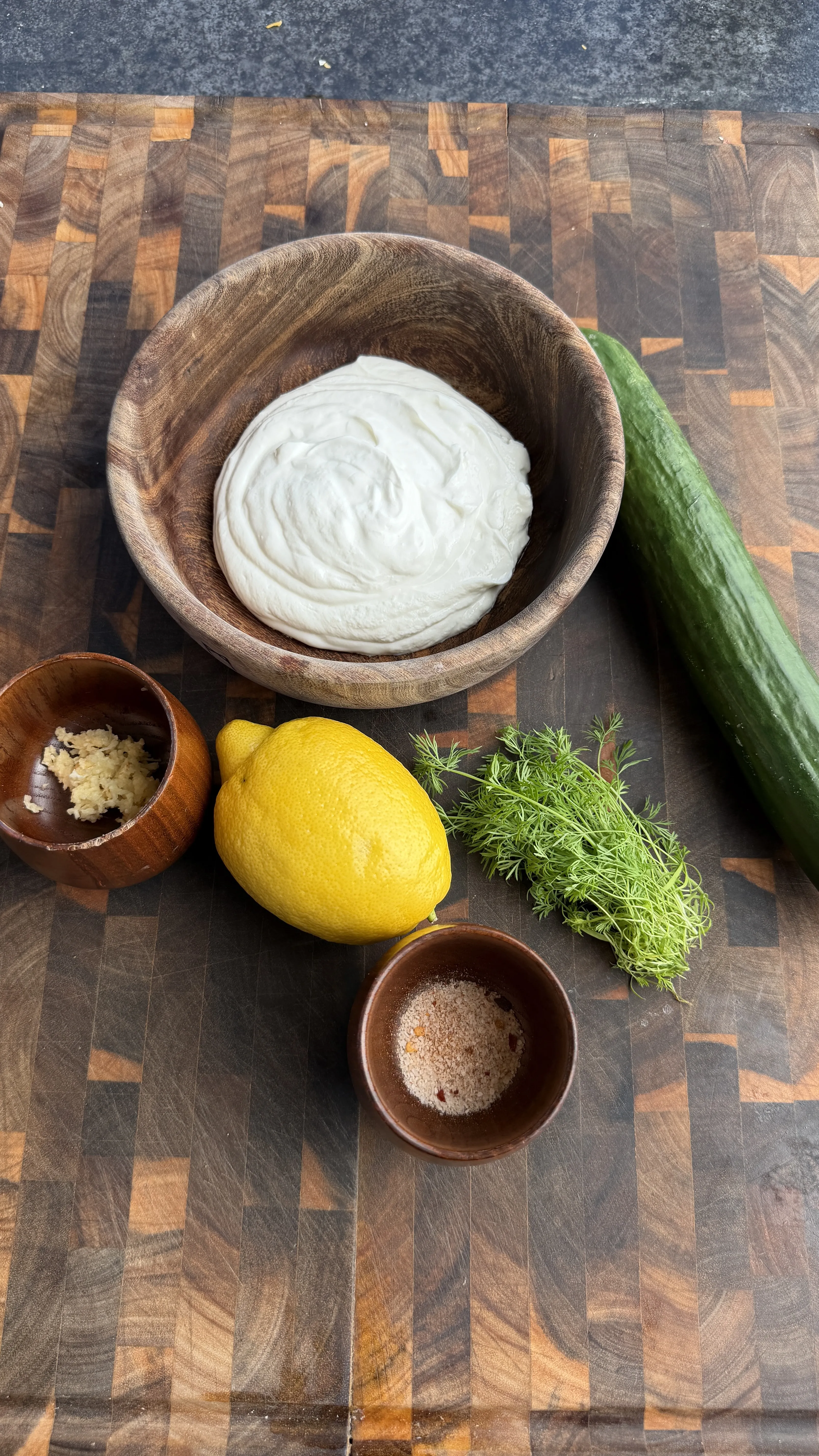 Ingredients for grilled lamb tortilla pinwheel skewers including yogurt sauce, cucumber, lemon, and herbs on cutting board