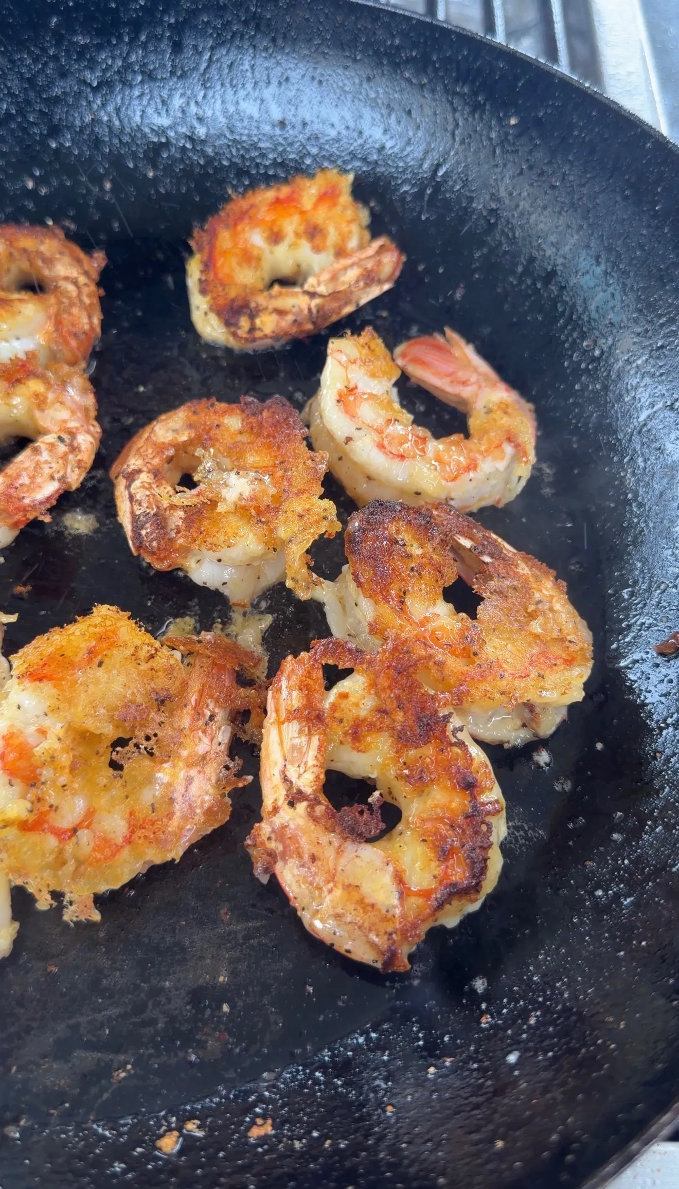 Golden brown lemon pepper crispy shrimp searing in a black cast iron pan with caramelized edges