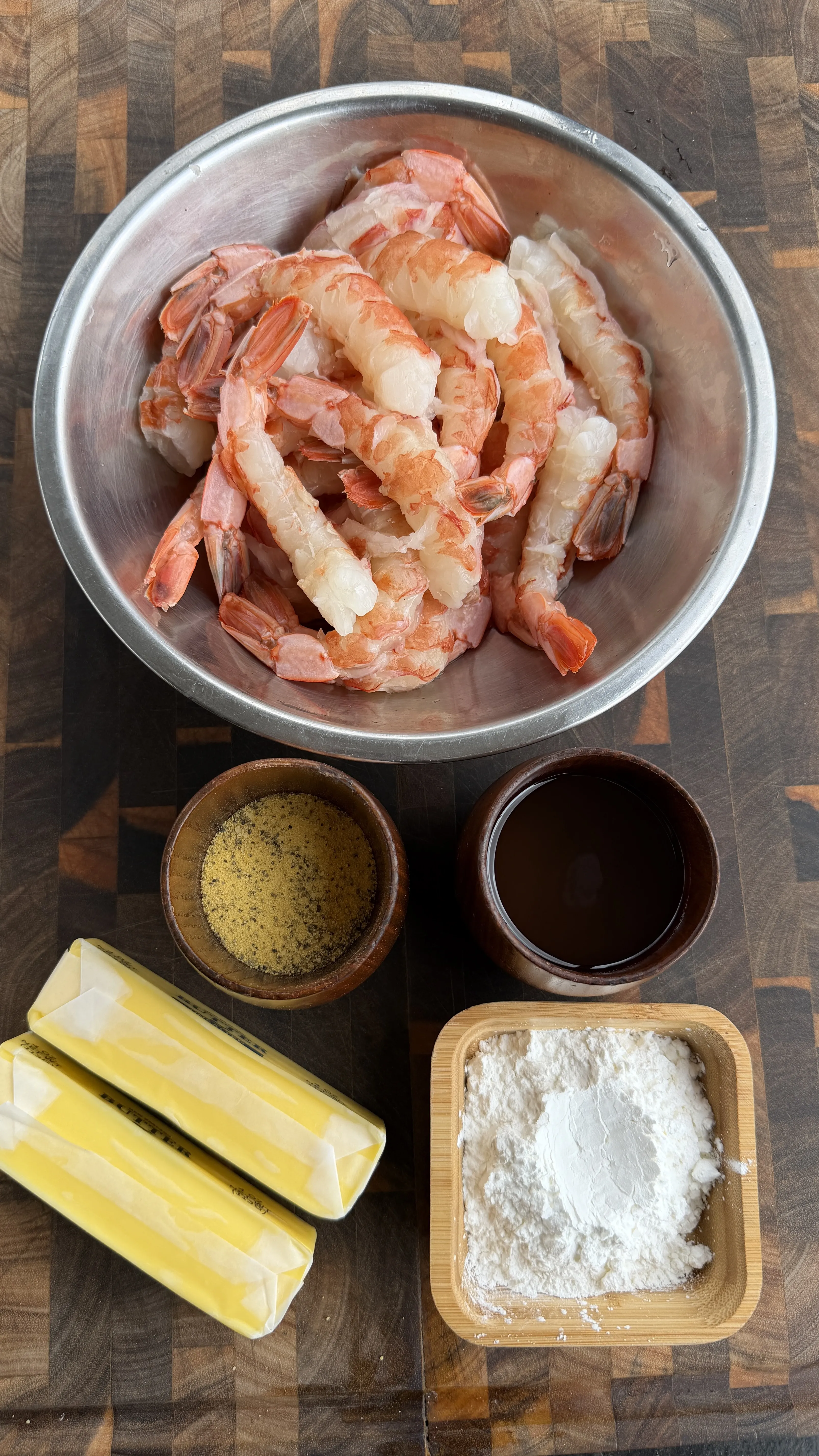 Raw peeled shrimp in metal bowl with flour, seasoning, butter, and dark sauce ingredients for lemon pepper crispy shrimp