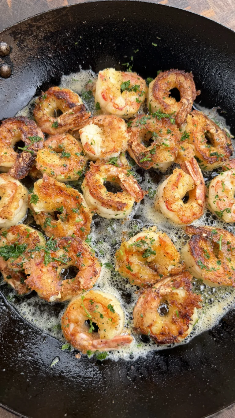 Golden lemon pepper shrimp sizzling in a black cast iron skillet with fresh herbs and butter