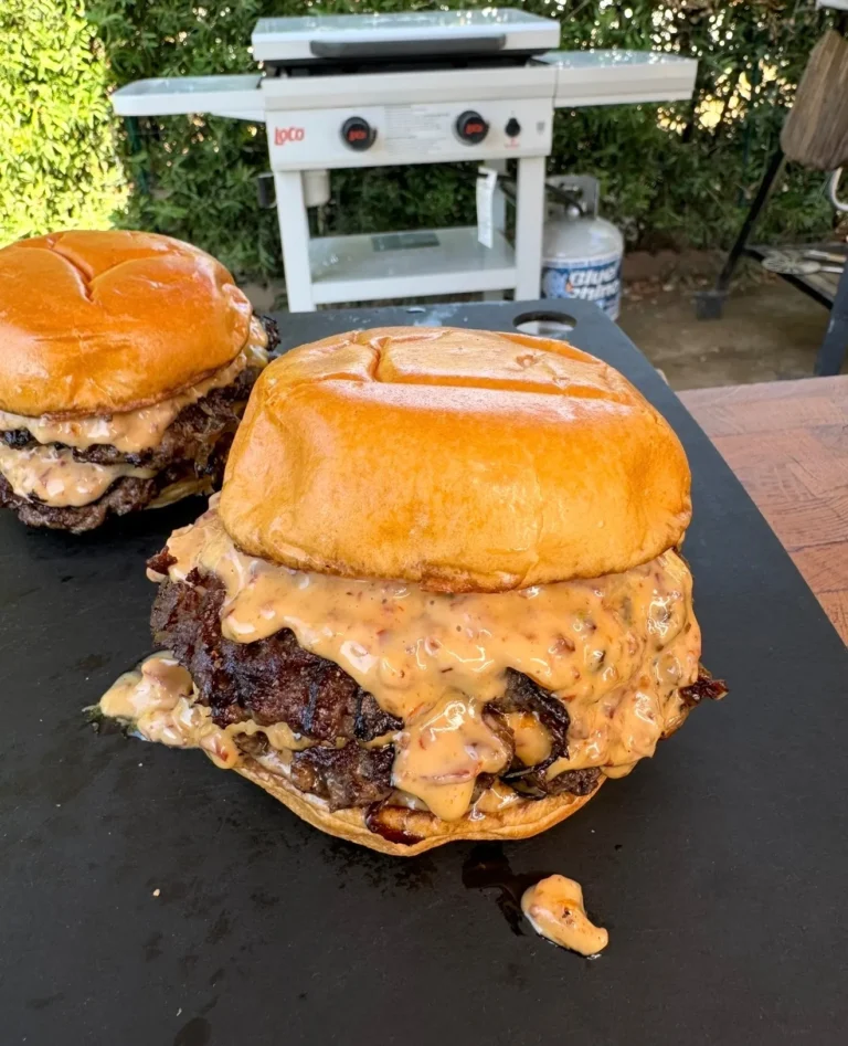 Two juicy smash burgers topped with melted cheese and baconnaise sauce on a black serving tray outdoors