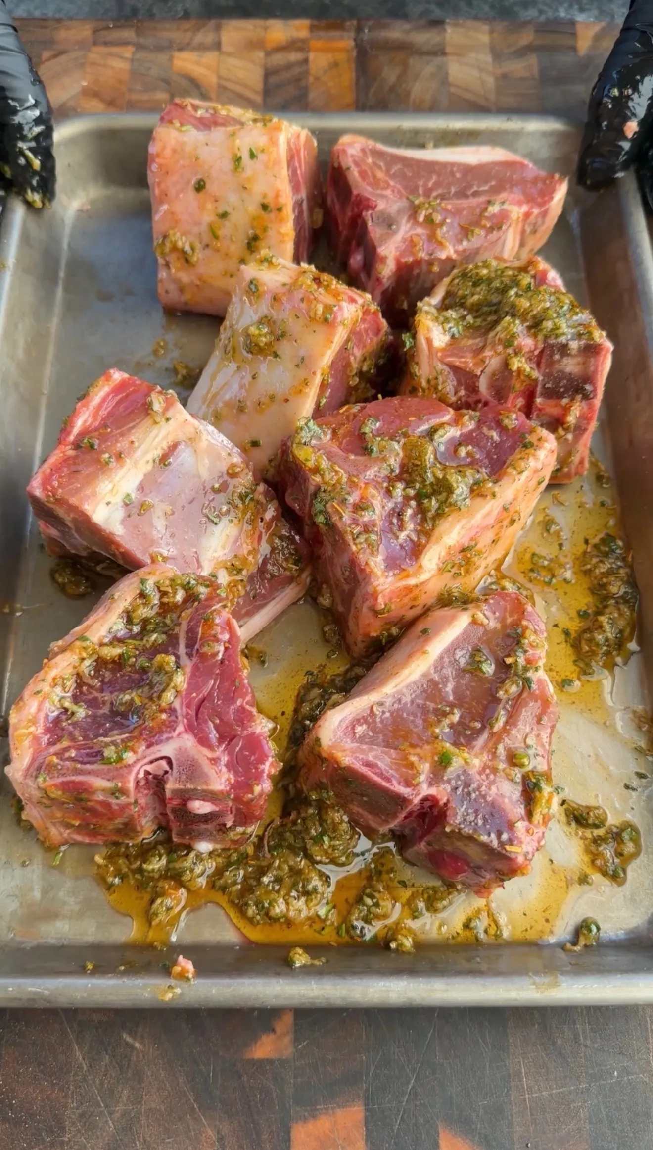 Raw lamb loin chops marinated with green herbs and garlic on a metal baking tray ready for grilling