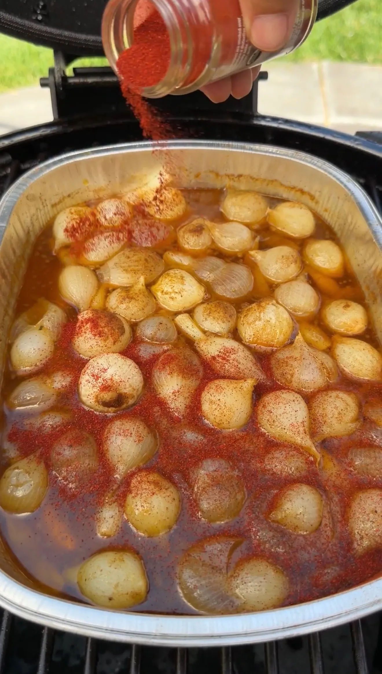 Mini Cajun onion boil cooking in pot with paprika being sprinkled on top of small onions in seasoned broth