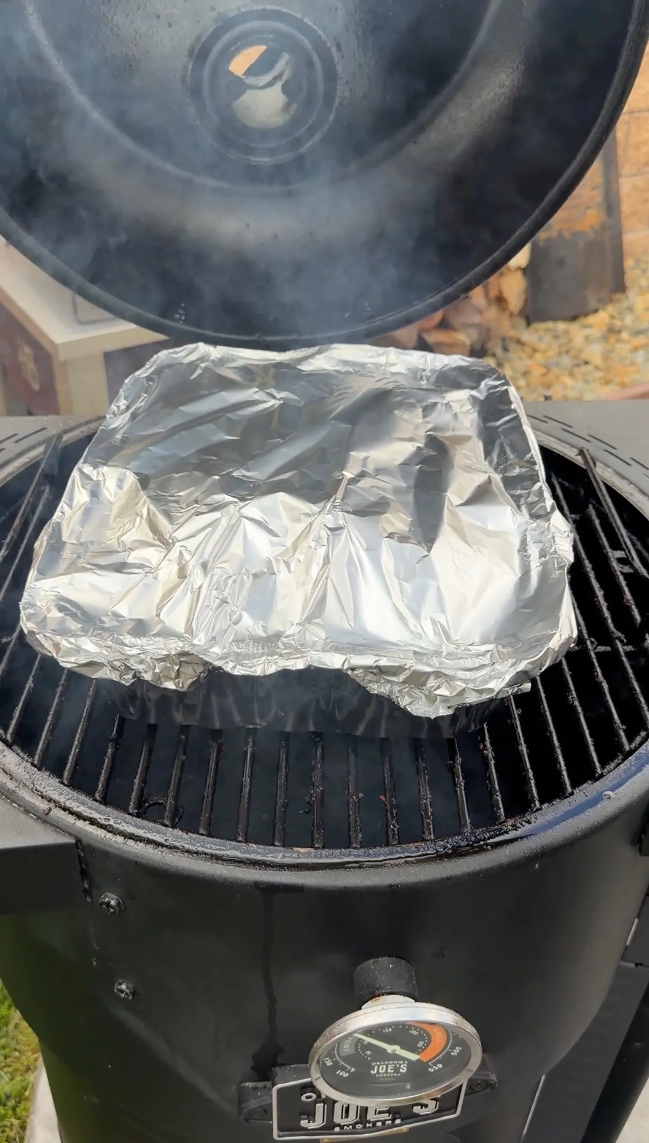Pork ribs in foil tray covered tightly with foil braising in molasses hot honey sauce on smoker