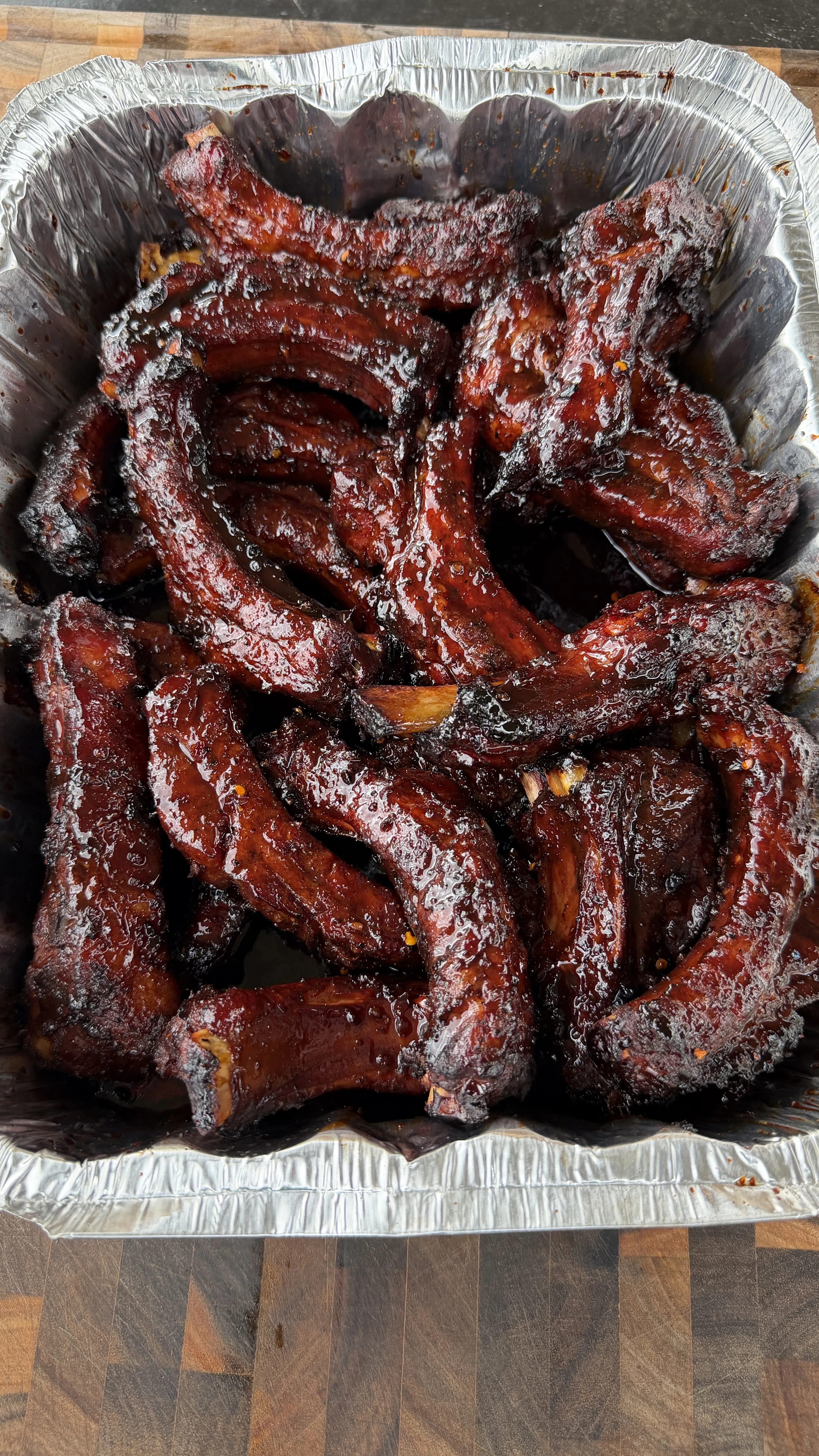Glazed molasses hot honey ribs in an aluminum pan with sticky dark sauce coating each rib