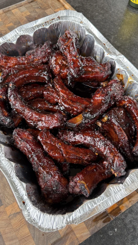 Molasses hot honey ribs with caramelized glaze in aluminum serving tray on wooden cutting board
