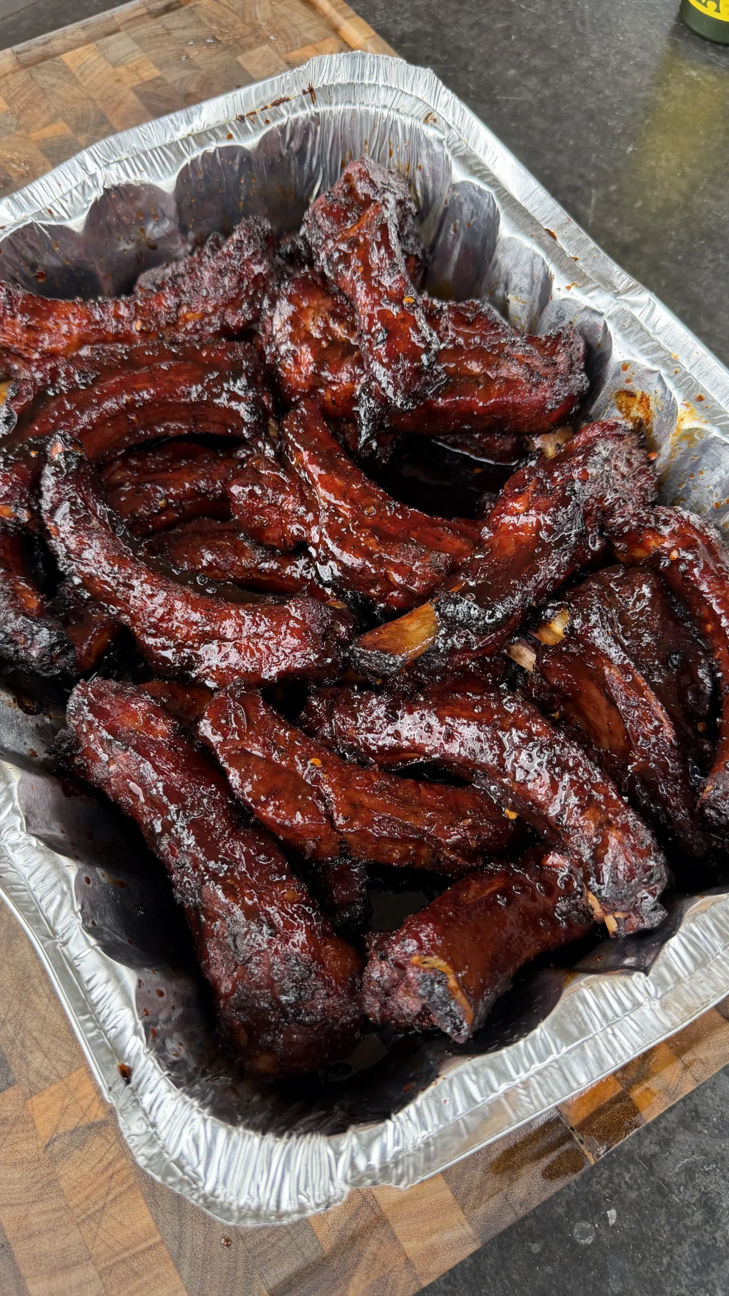Molasses hot honey ribs with caramelized glaze in aluminum serving tray on wooden cutting board