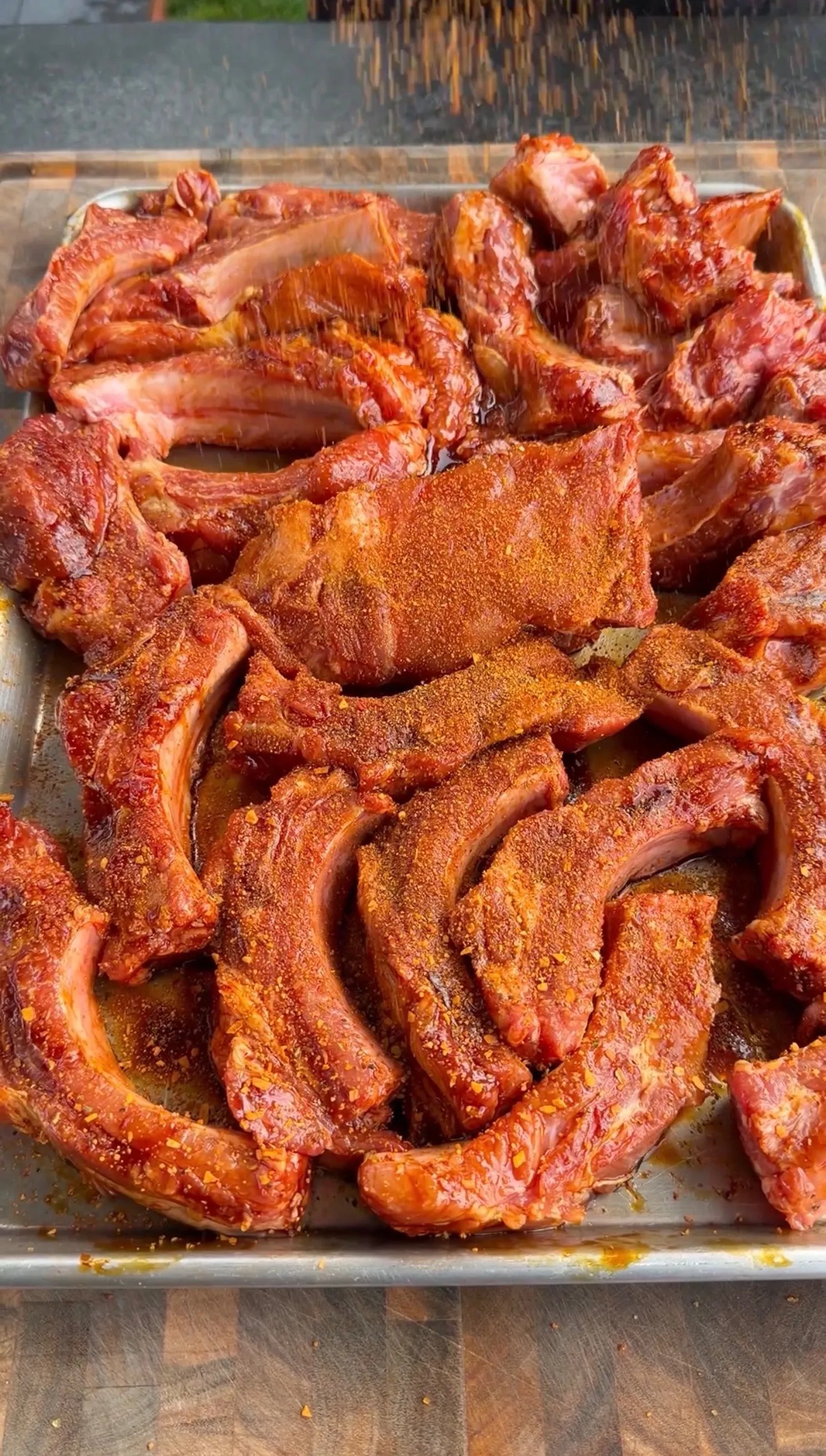 Individual pork ribs seasoned with BBQ rub and molasses binder arranged on a metal tray