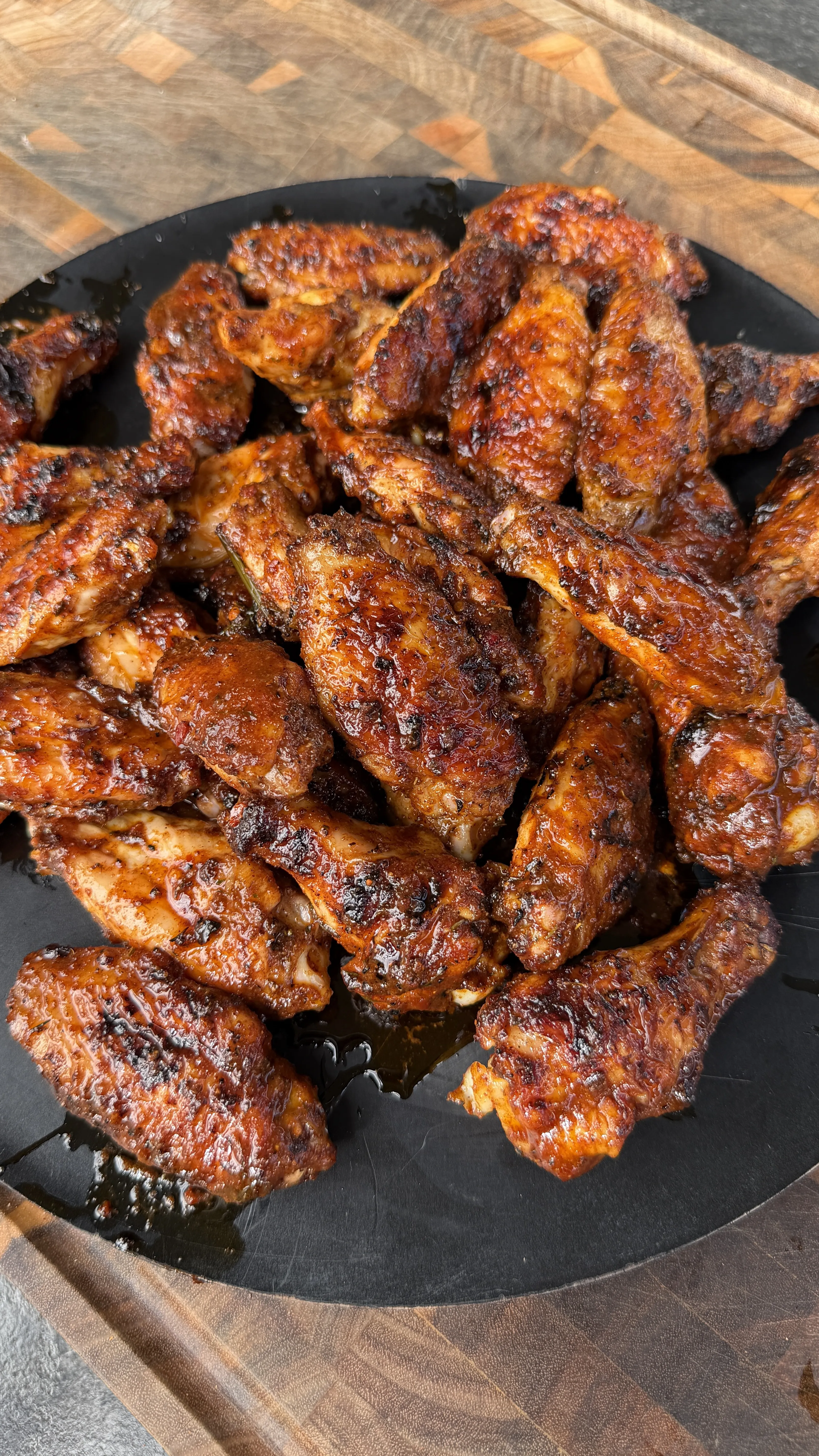 Nashville hot pickle brined chicken wings with caramelized glaze in a black cast iron skillet on wooden board
