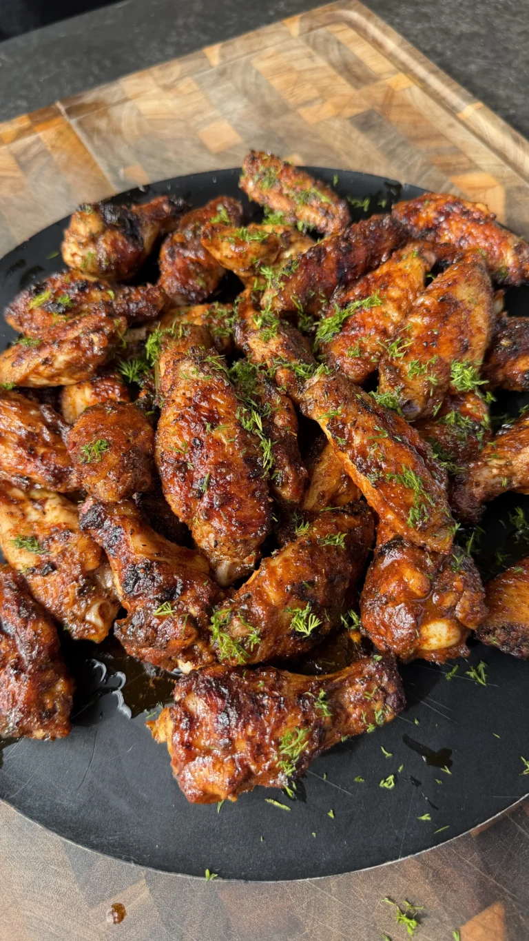 Golden brown Nashville hot pickle brined chicken wings in a black cast iron skillet garnished with fresh herbs