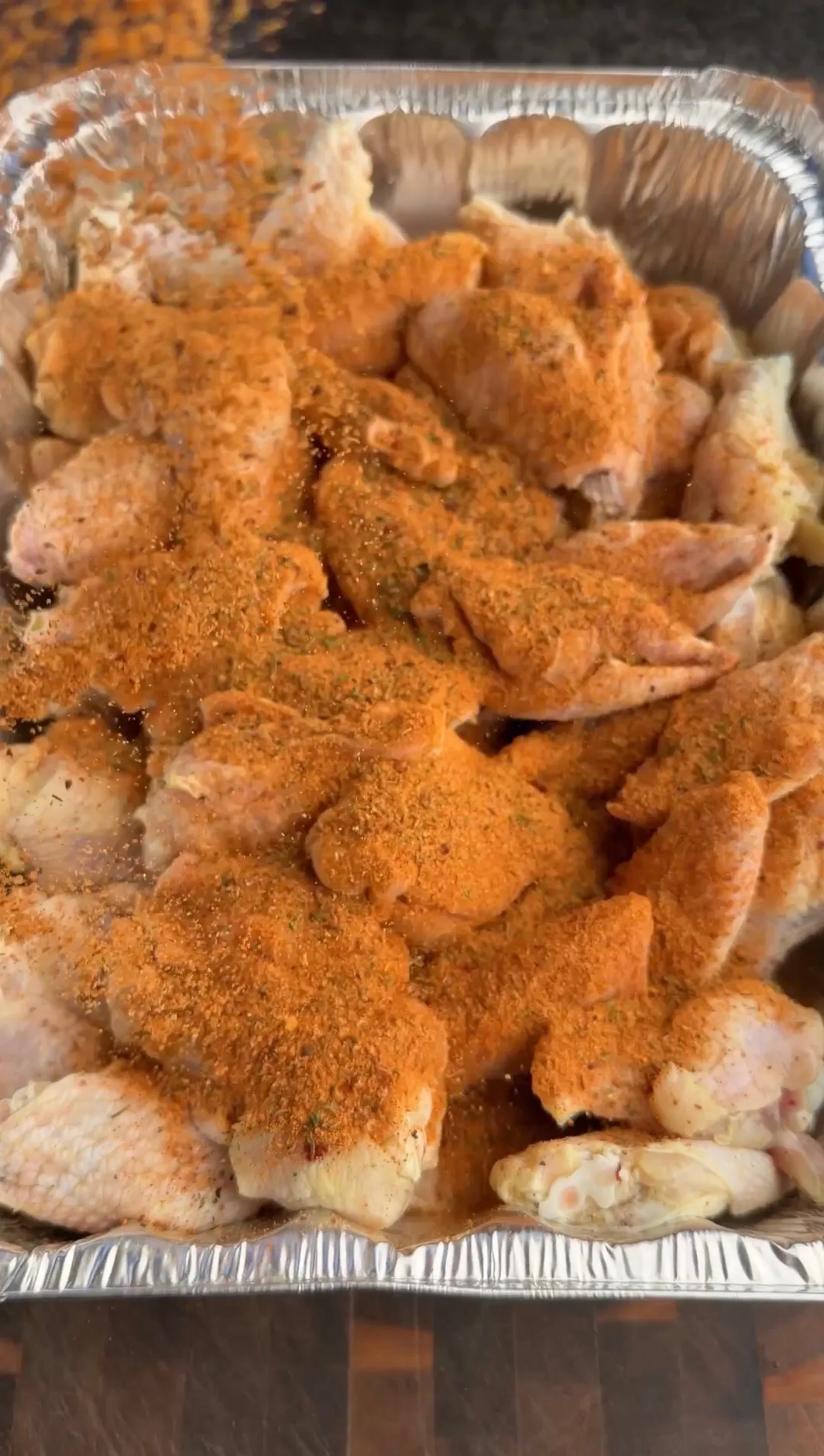 Raw chicken wings coated in orange Nashville hot seasoning and spices in aluminum foil pan ready for cooking