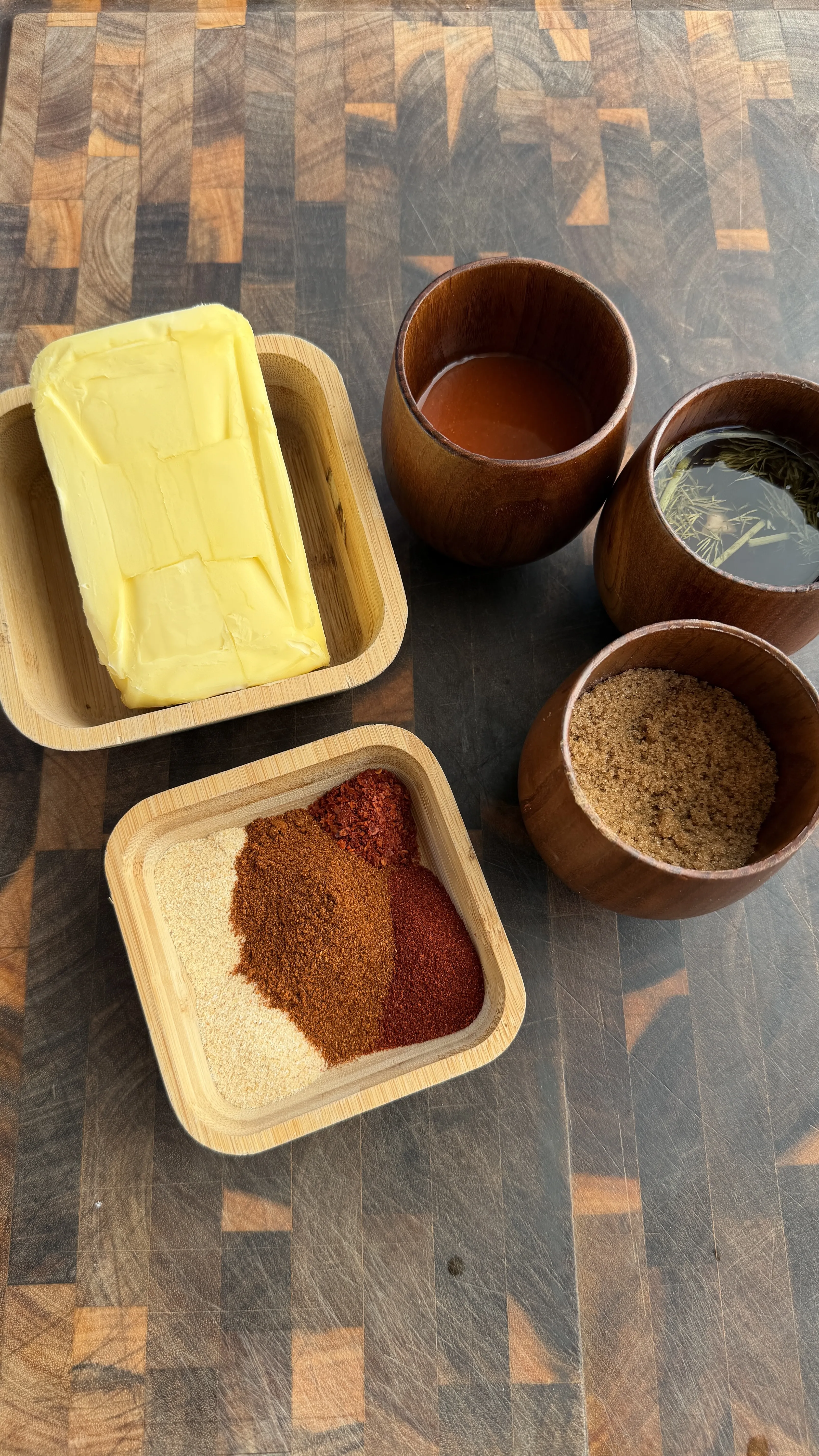 Nashville hot wing ingredients in wooden bowls including butter, spices, and pickle brine on cutting board