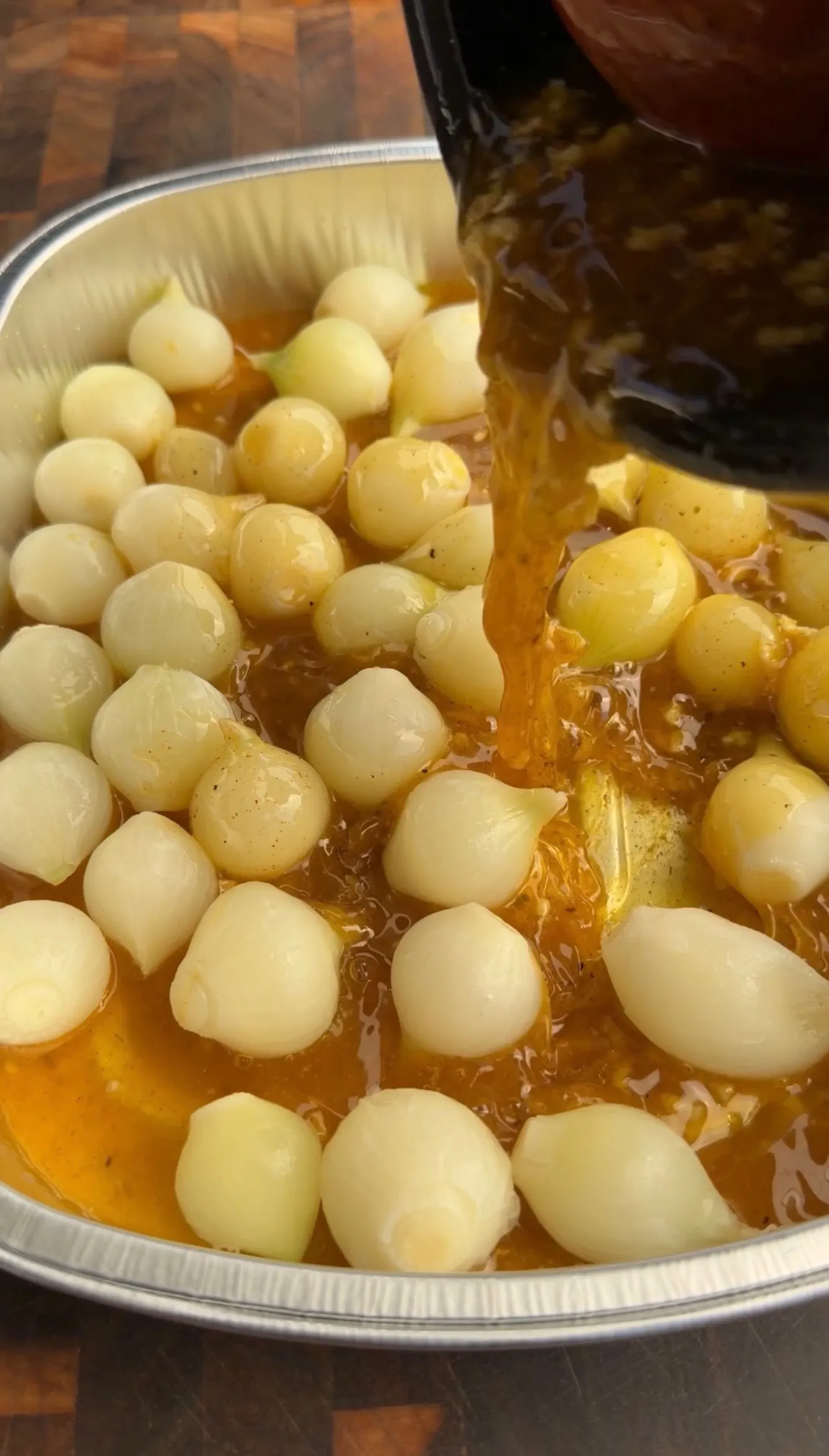 Pearl onions simmering in golden Cajun broth being poured from ladle in aluminum pot
