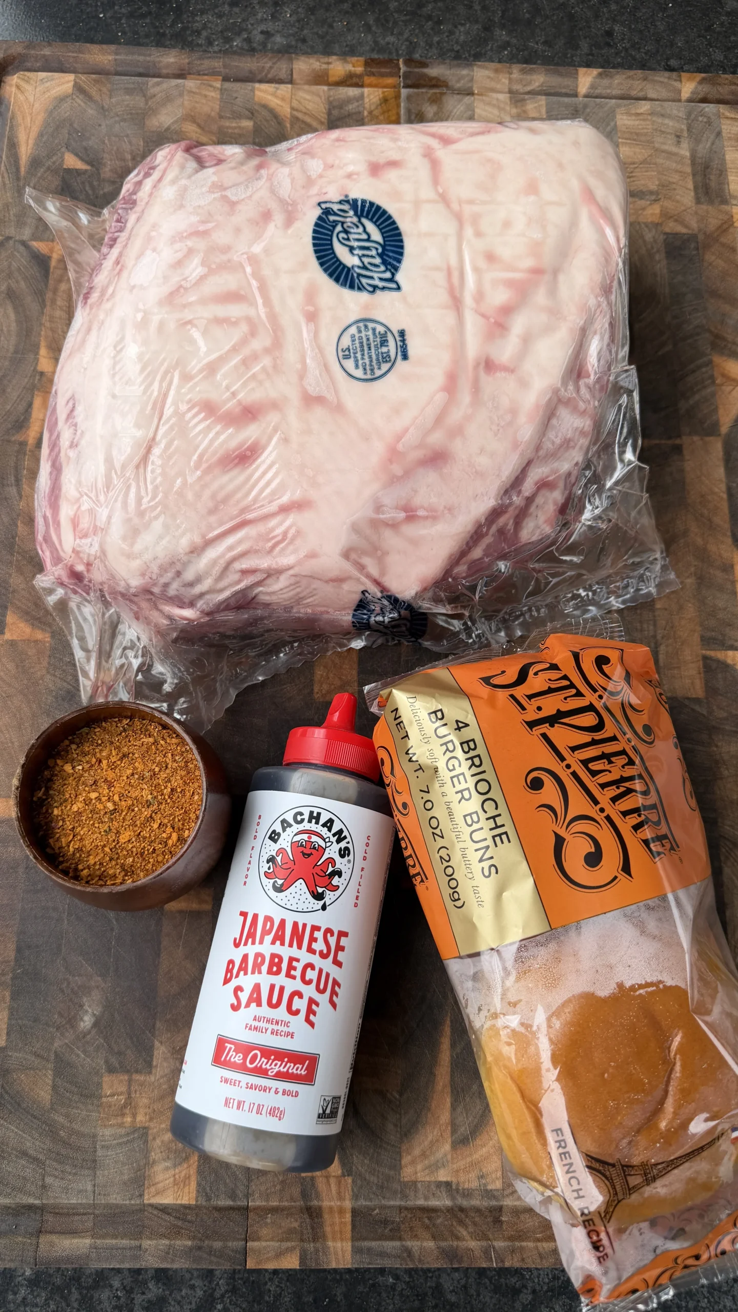 Raw pork shoulder, Japanese barbecue sauce, burger buns, and spice blend arranged on wooden cutting board