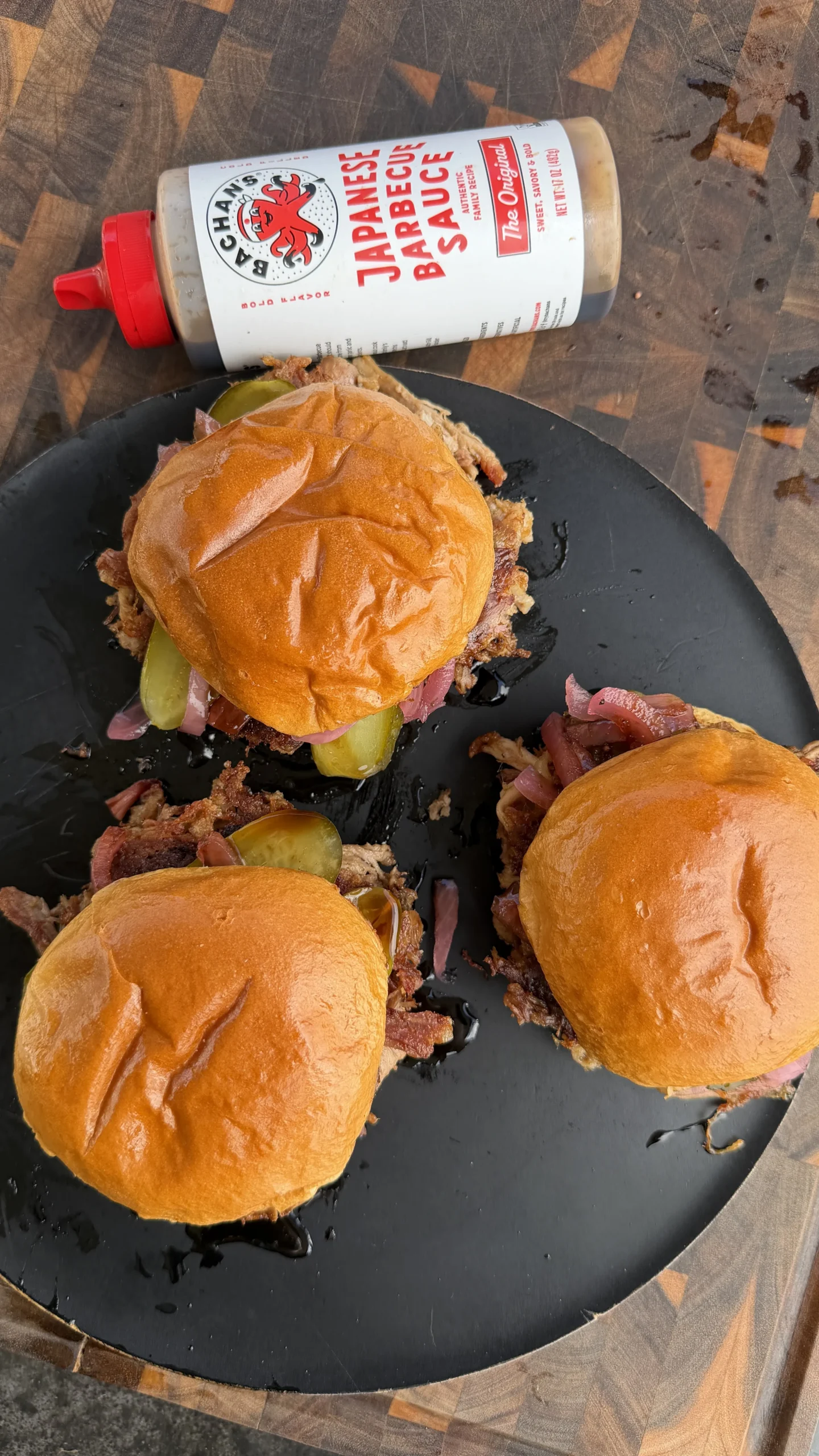 Three pulled pork smashburgers with pickles and red onions cooking in a black cast iron skillet