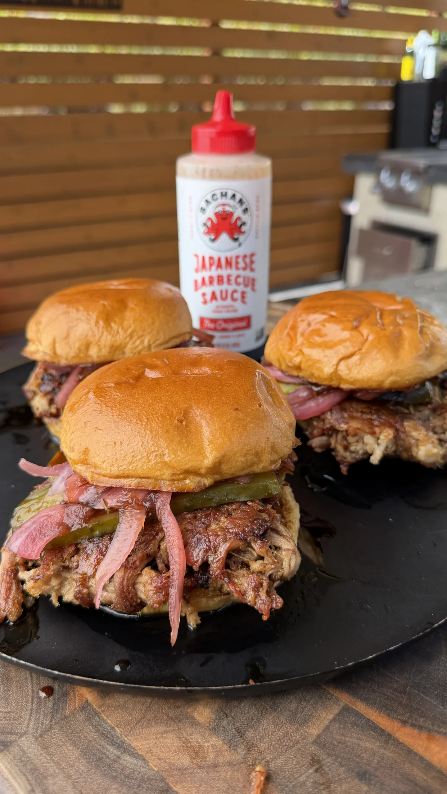 Three pulled pork smashburgers with pickled onions on brioche buns, served with Japanese barbecue sauce