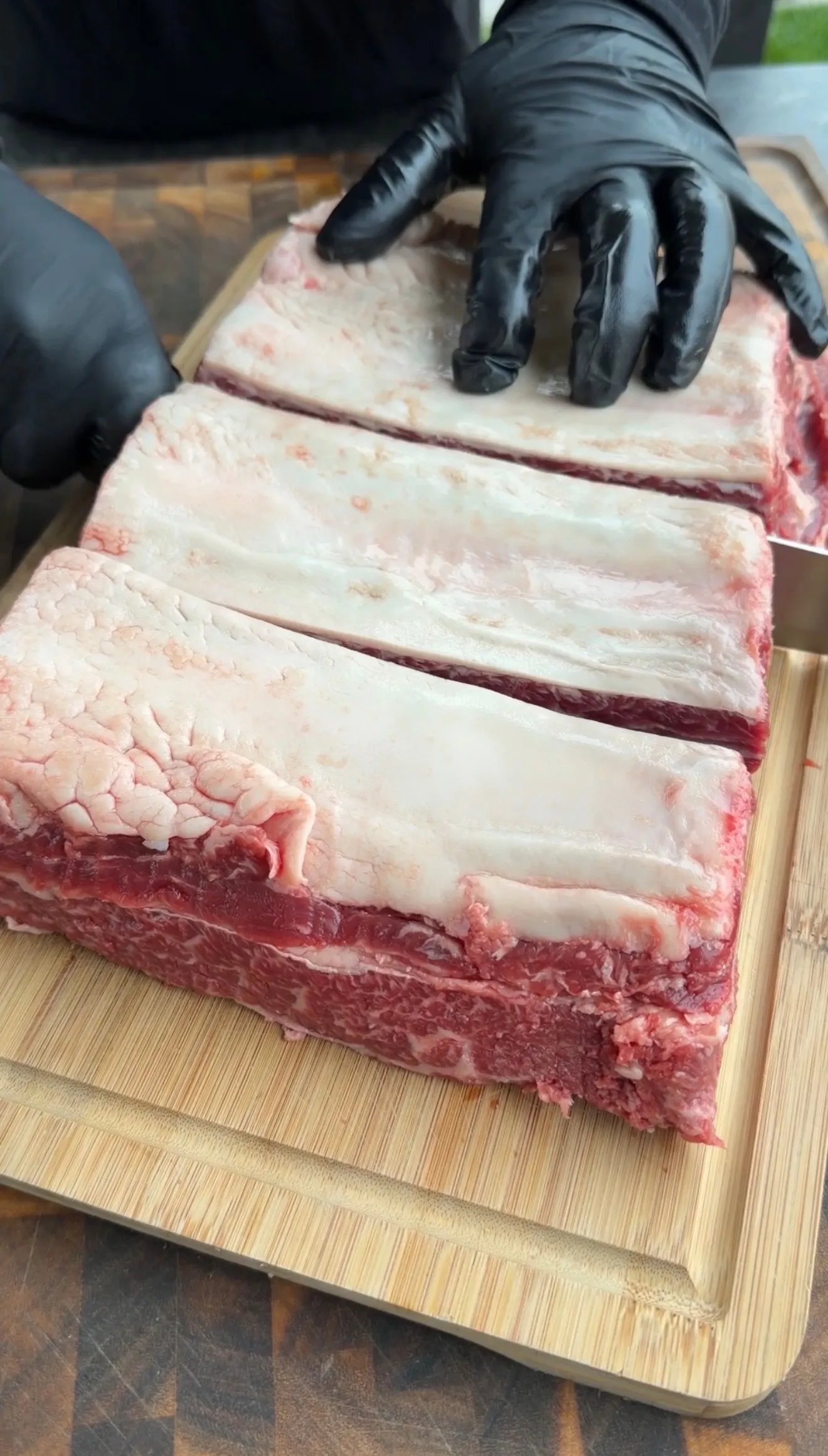 Raw beef ribs being scored with knife on wooden cutting board