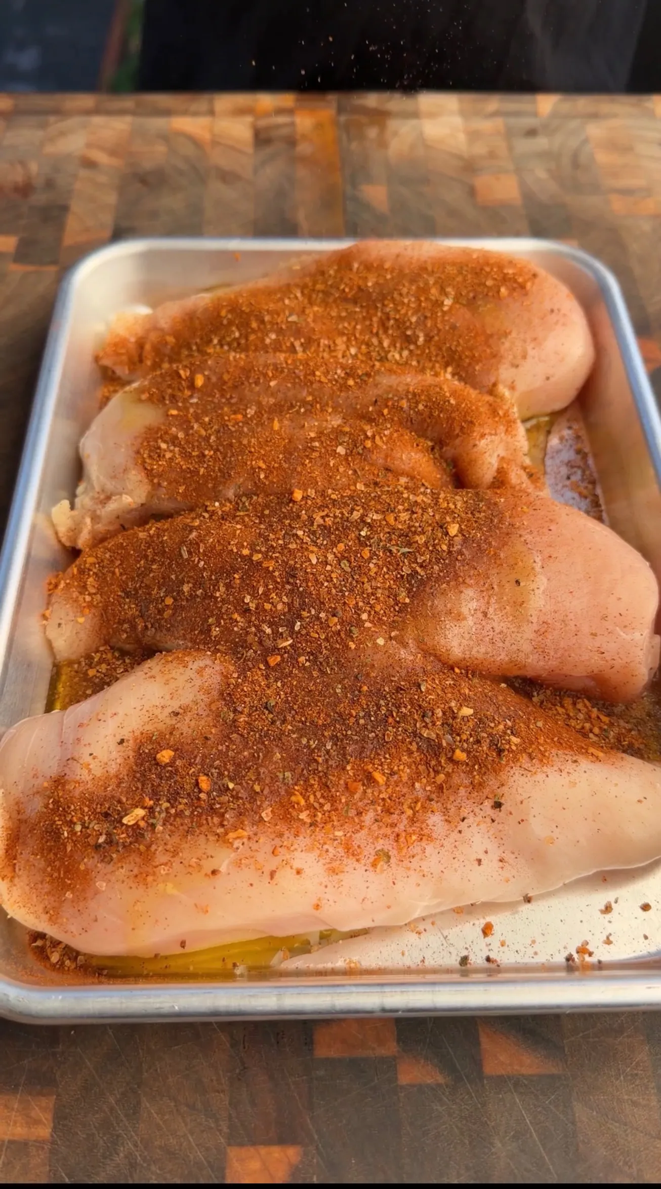 Raw chicken breasts coated with Cajun spice blend in a white baking dish on wooden cutting board