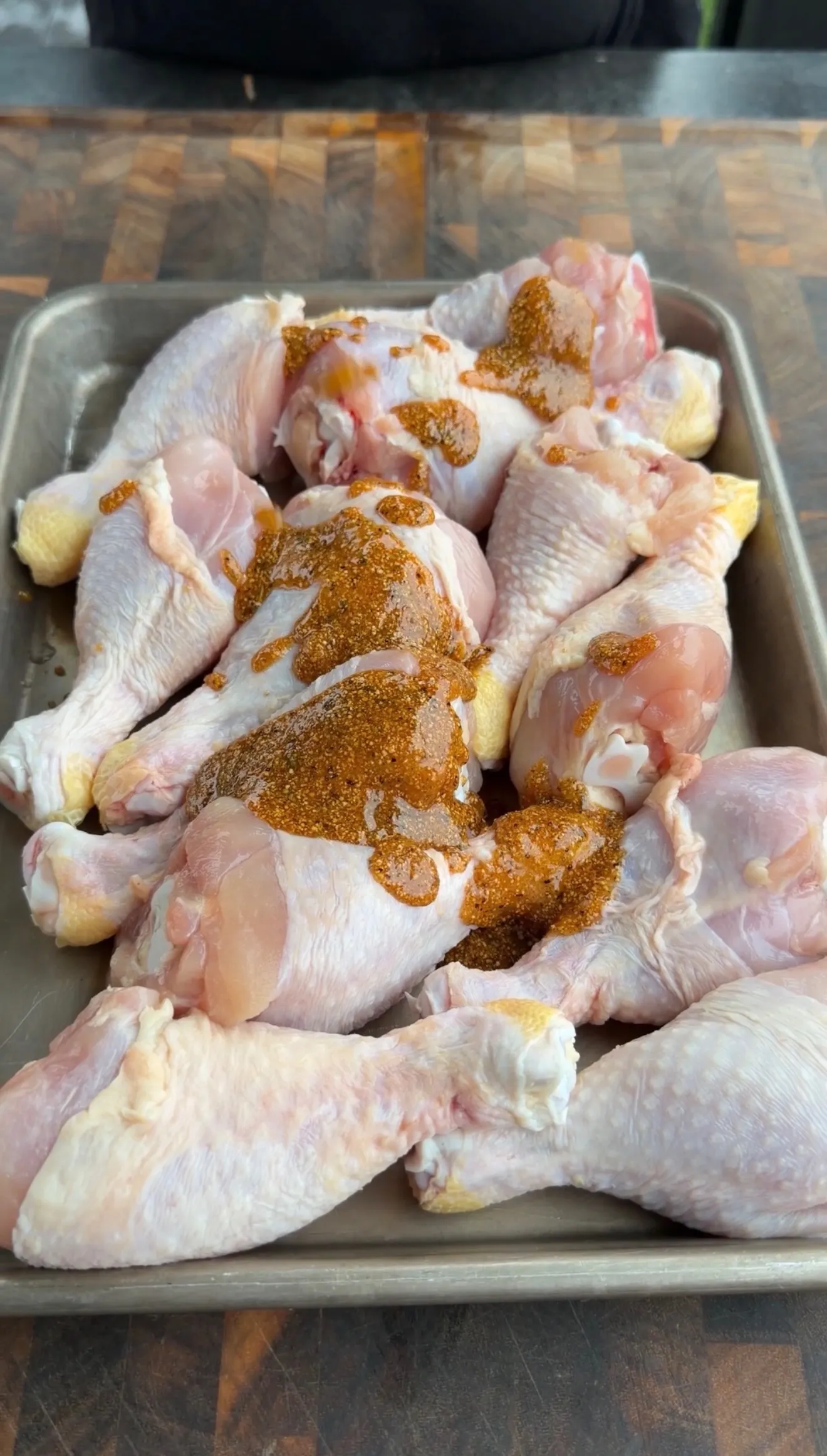 Raw chicken drumsticks coated with barbecue spice rub in metal baking pan ready for cooking