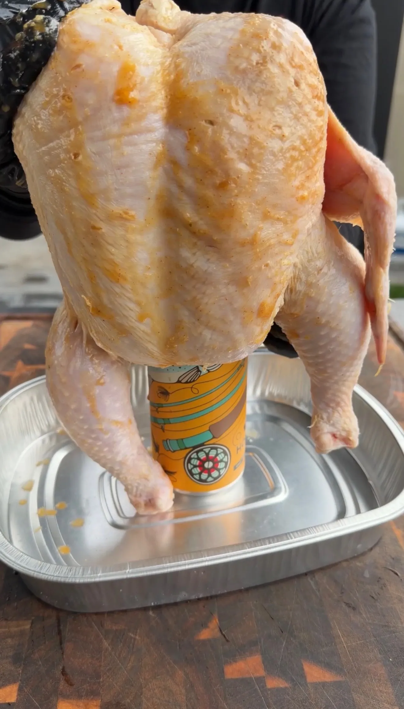 Raw whole chicken positioned over a beer can in aluminum pan, ready for grilling beer can chicken recipe