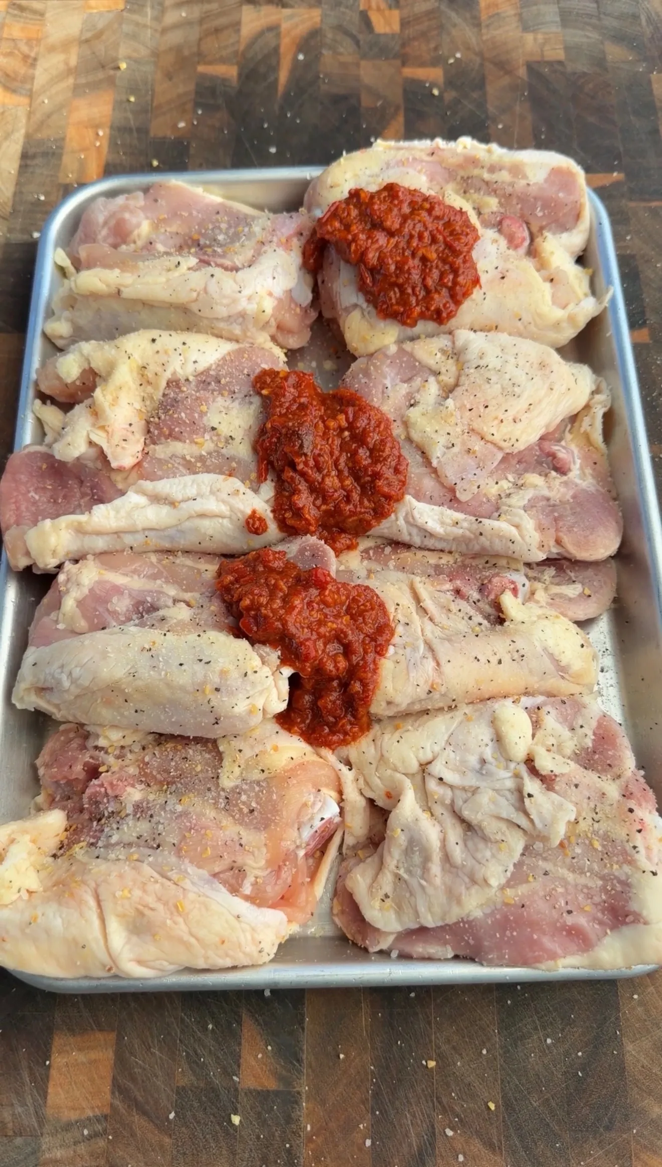 Raw chicken thighs coated in harissa marinade in baking pan