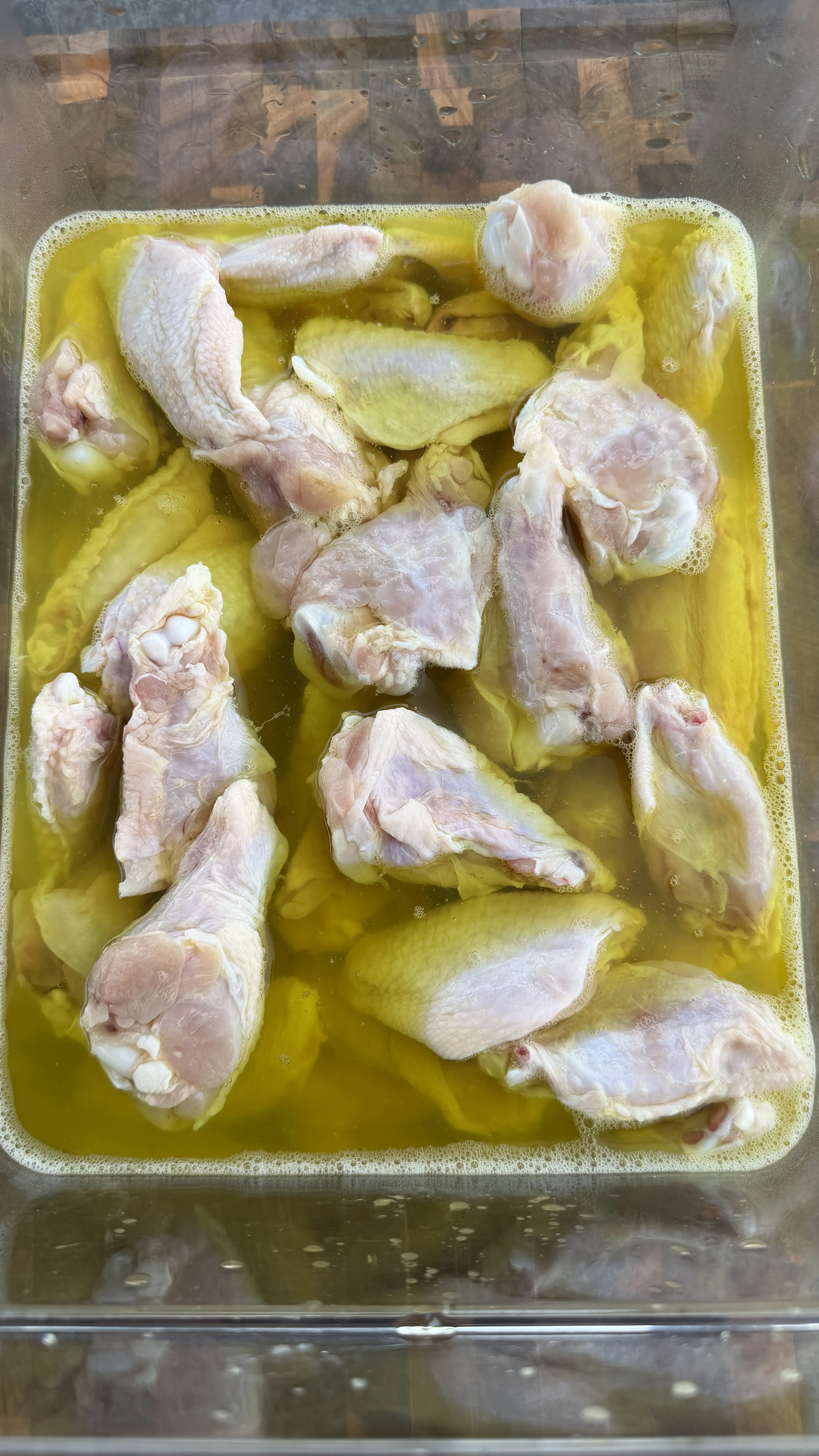 Raw chicken wings marinating in yellow pickle brine in aluminum tray for Nashville hot wings recipe