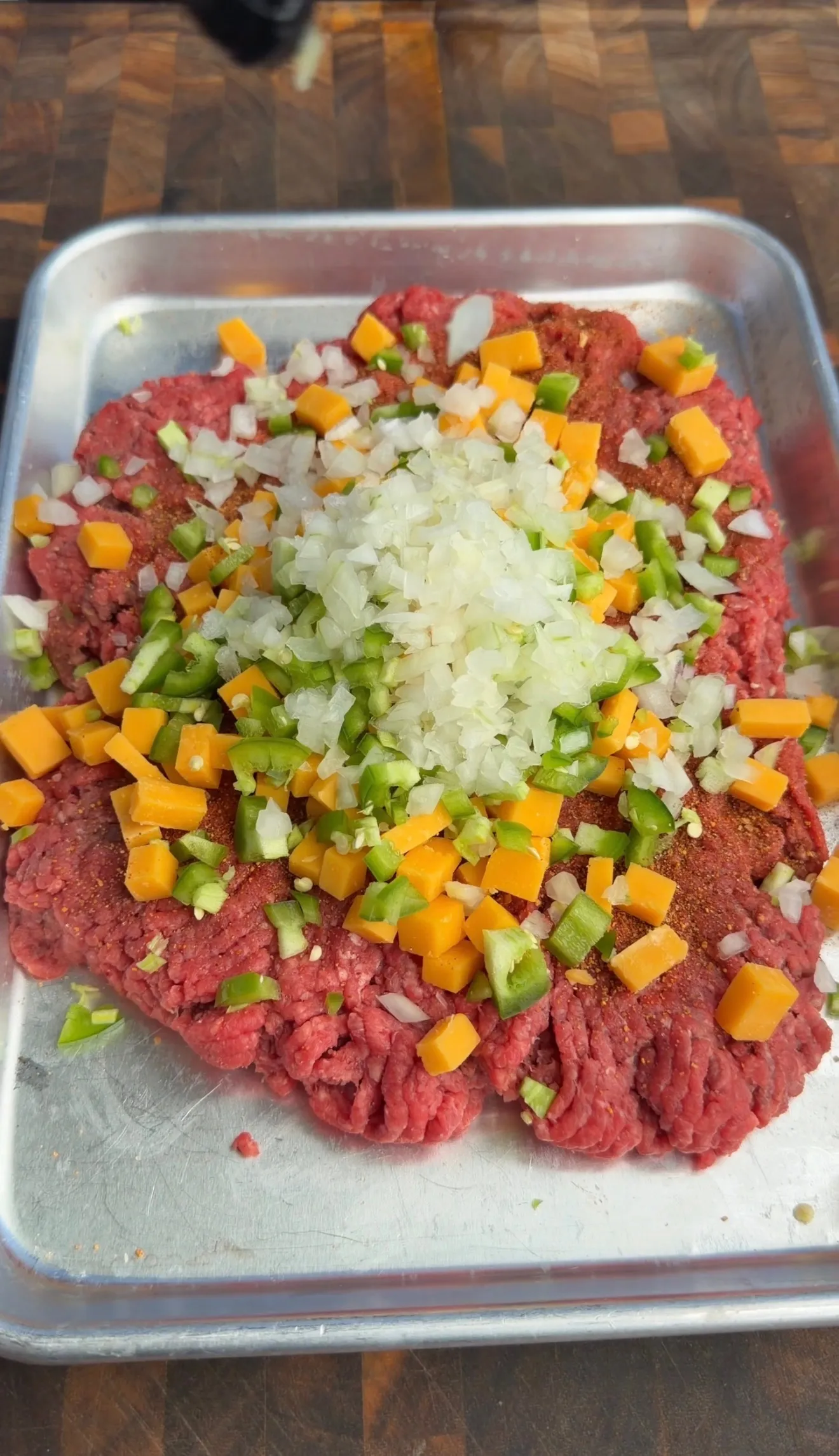 Raw ground beef with diced onions, carrots, and celery in a metal mixing bowl for stuffed burger preparation