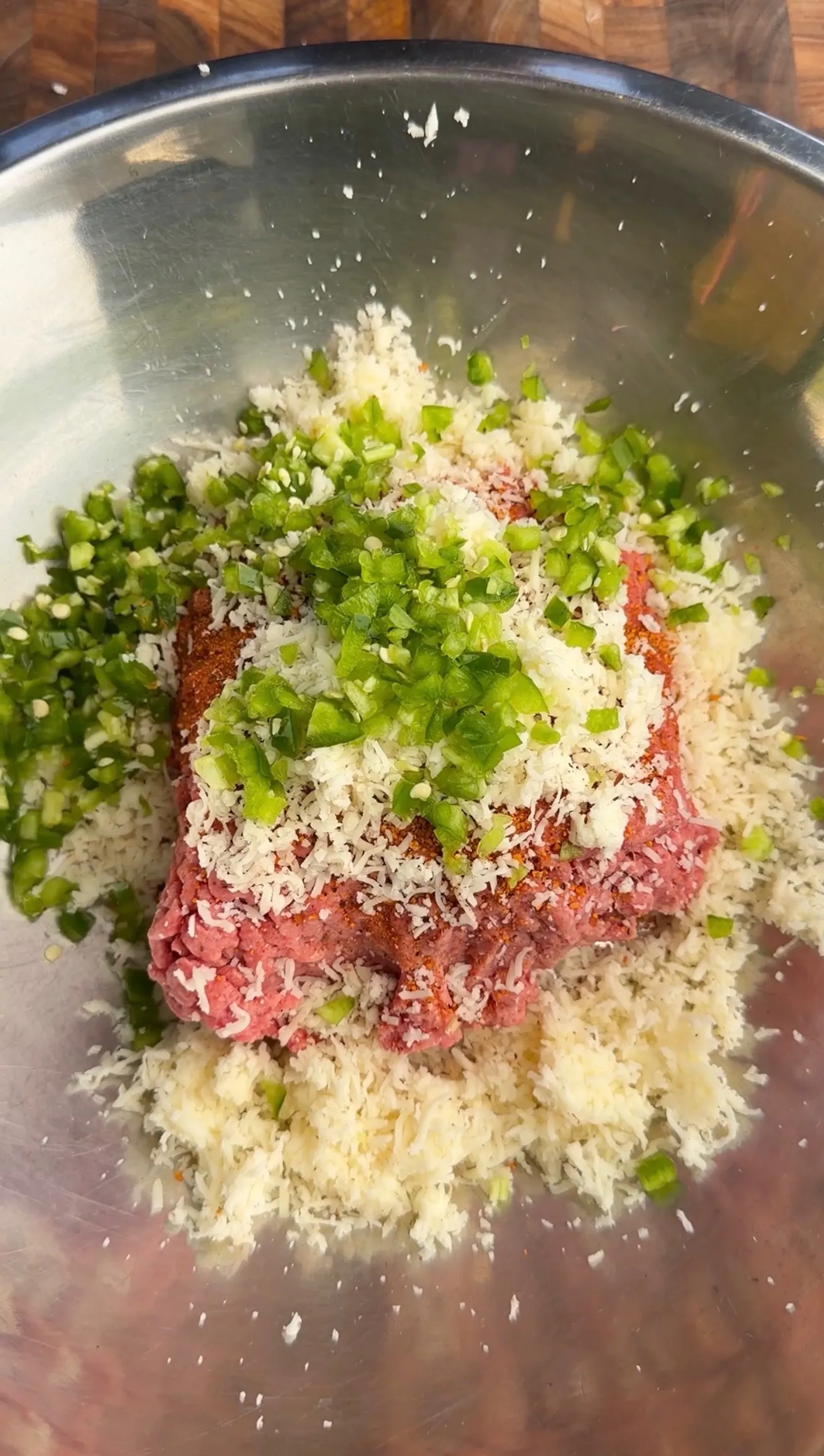 Raw ground beef mixed with fresh herbs and grated cheese in a stainless steel bowl for jalapeño beef skewers