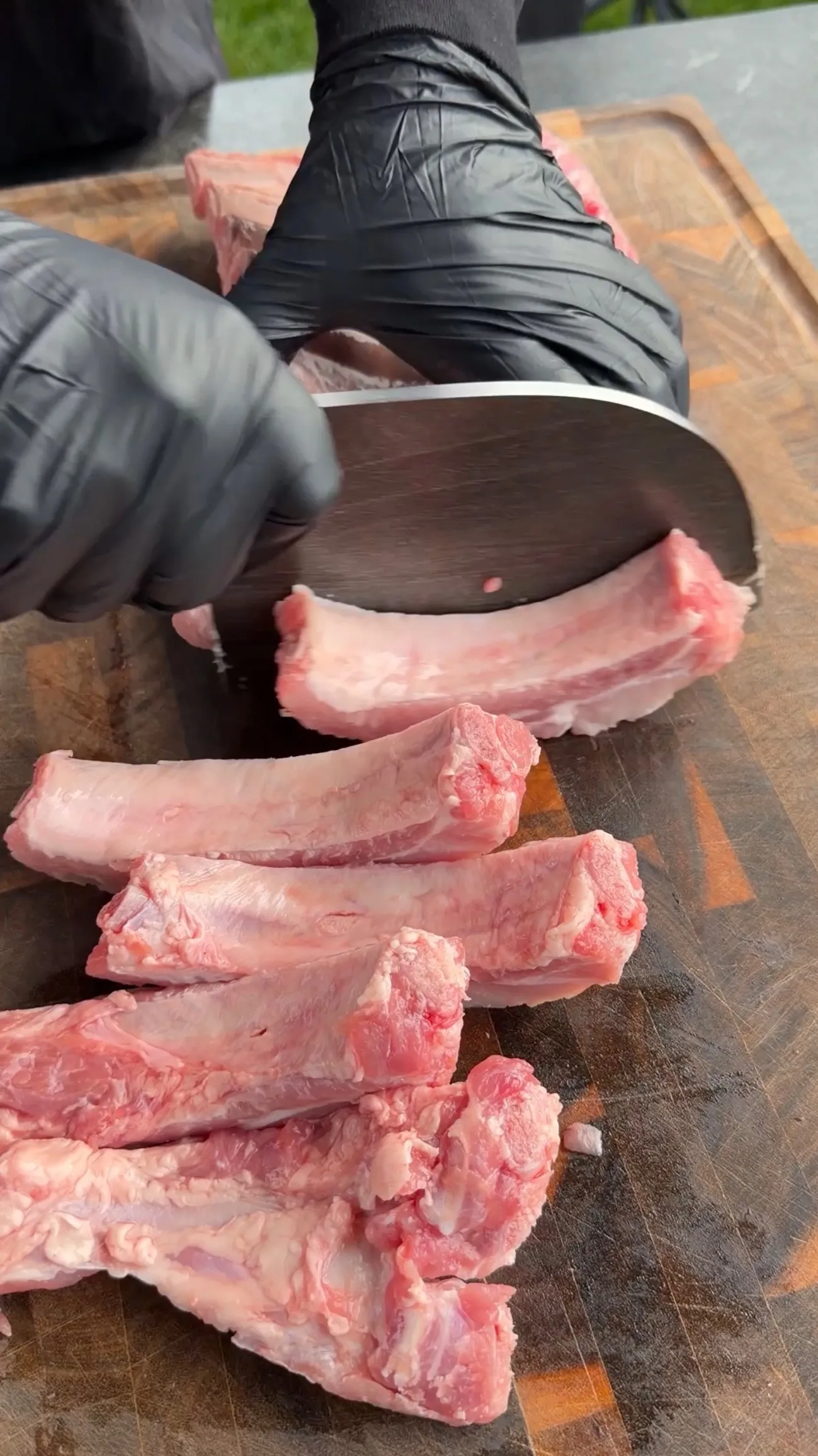 Raw pork ribs being cut between the bones into individual ribs on a wooden cutting board