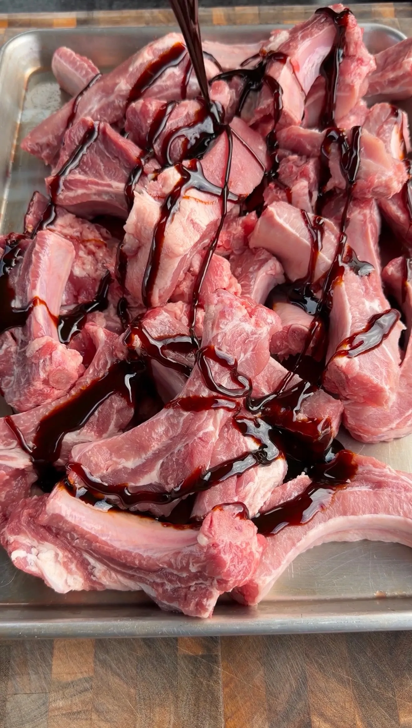 Raw pork ribs coated with dark molasses honey marinade in a baking dish before smoking