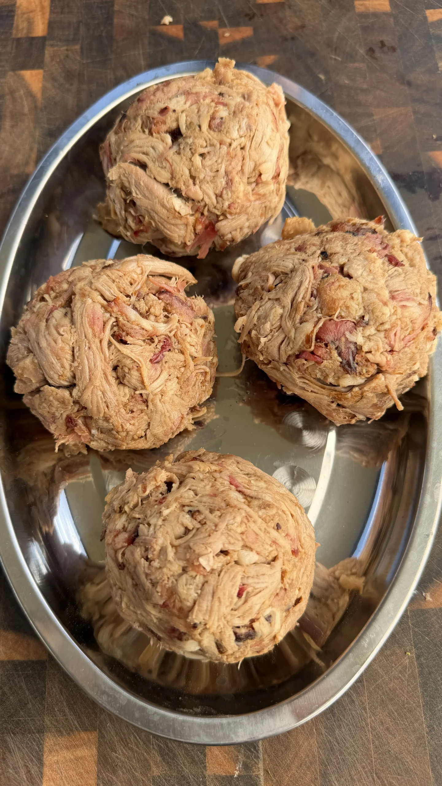 Four raw pulled pork smashburger patties formed and ready to cook in a stainless steel bowl