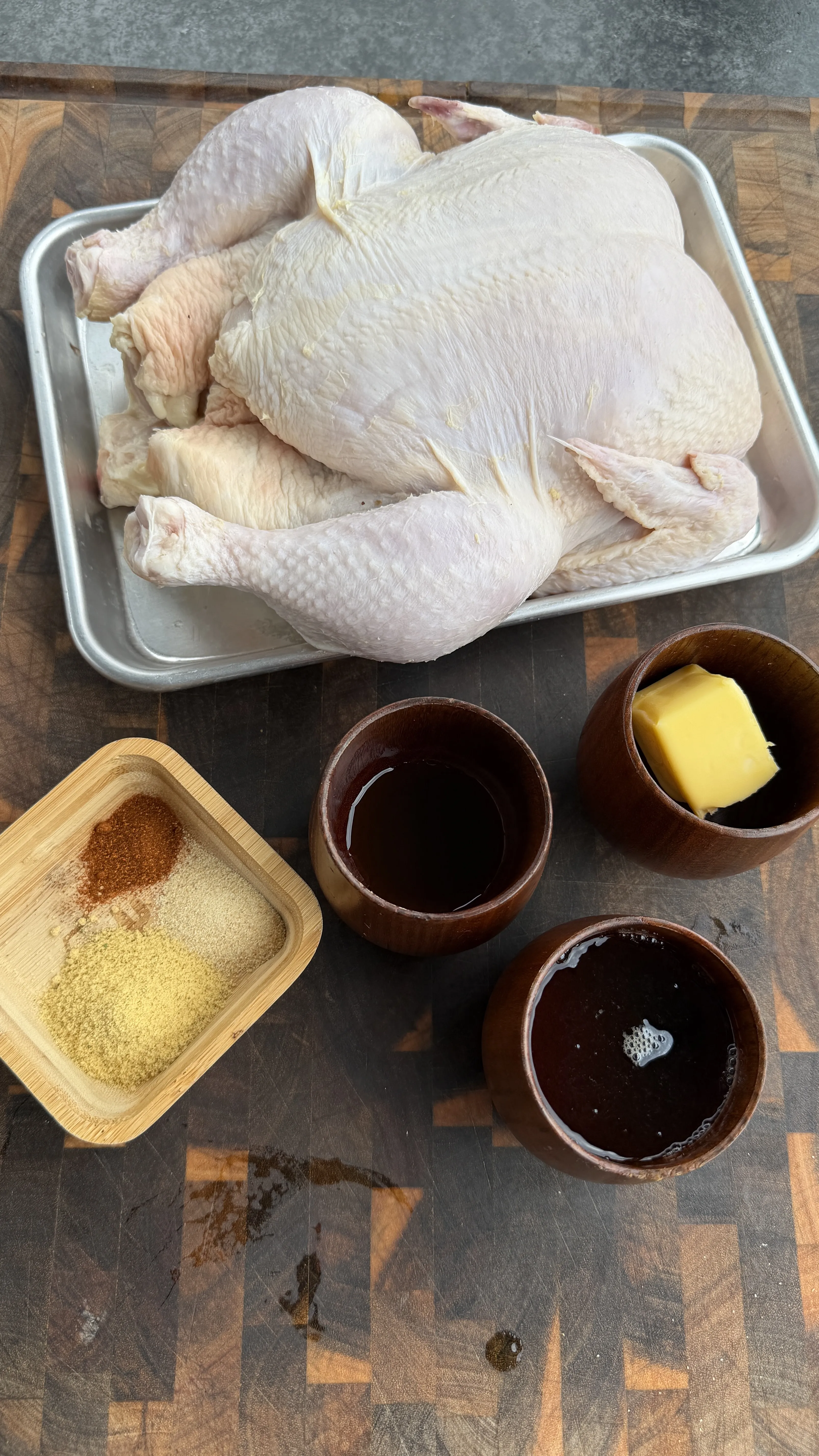 Raw whole chicken in metal pan with spices, butter, and dark beer in bowls for beer can chicken preparation