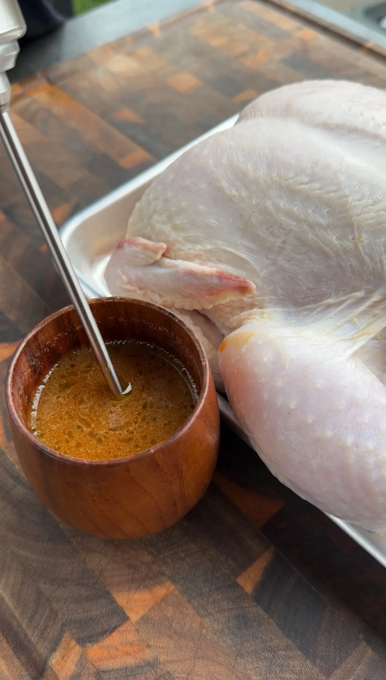 Raw whole chicken on metal tray next to wooden bowl of beer marinade with spoon for beer can chicken recipe