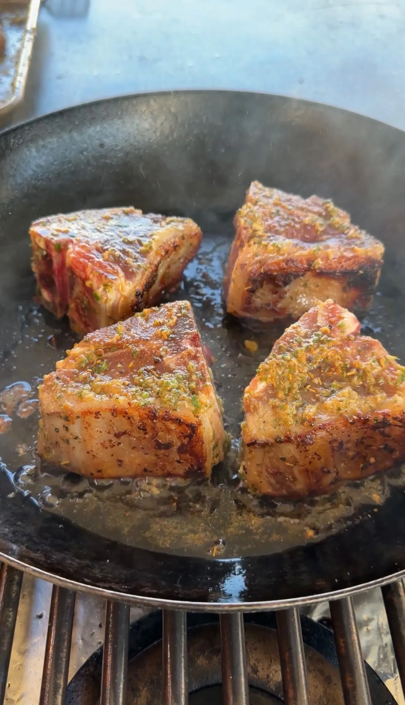 Four seasoned lamb loin chops searing in a black cast iron skillet with herbs and garlic