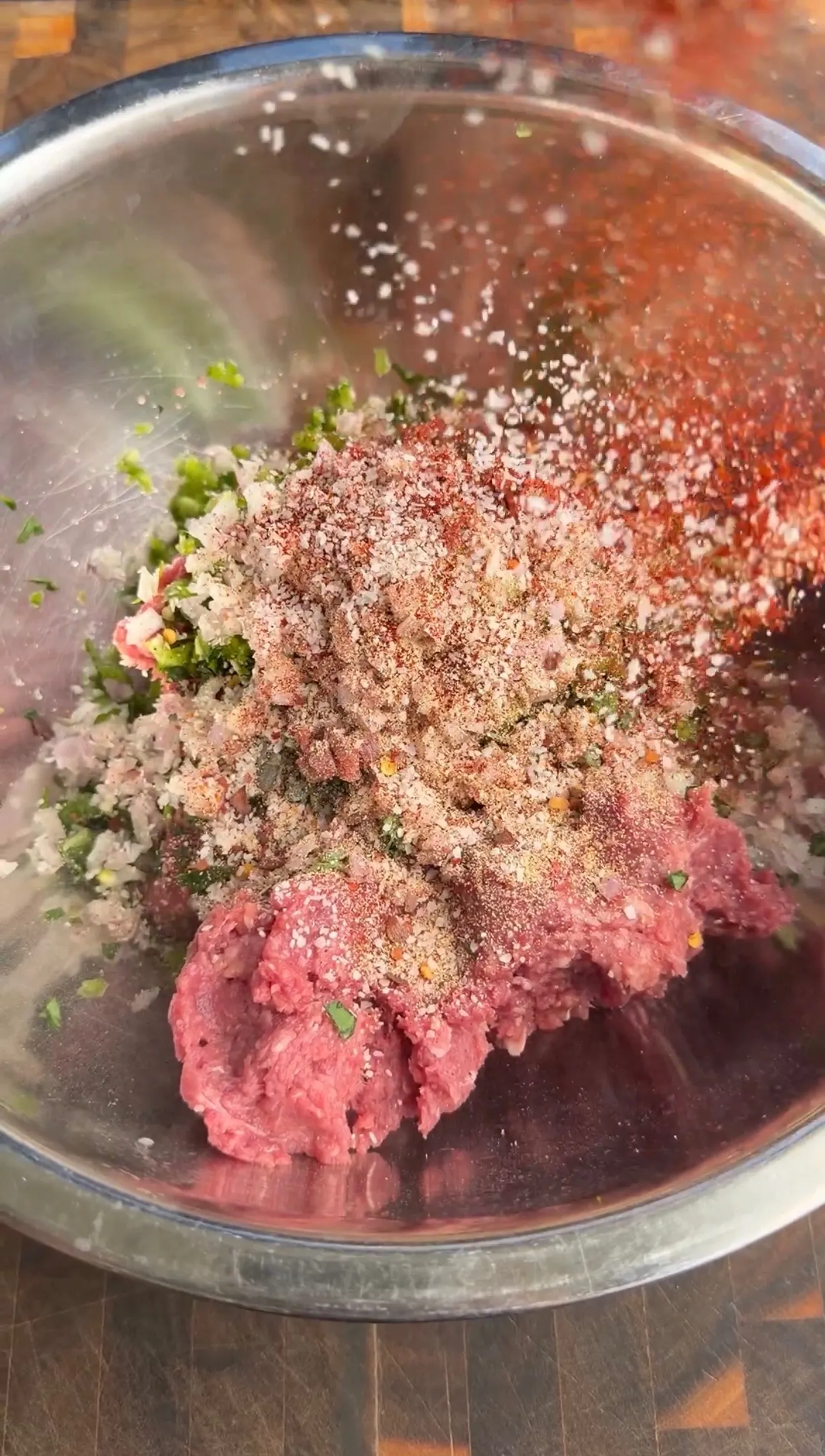 Raw seasoned ground lamb with herbs and spices being mixed in a stainless steel bowl