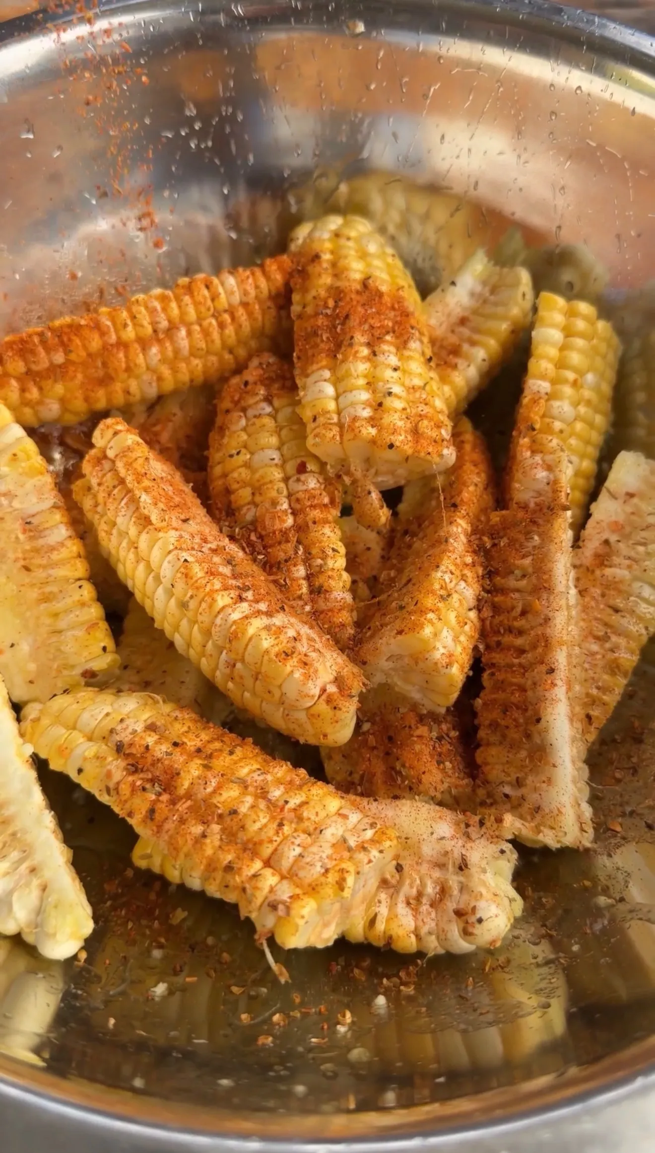 Golden mini corn ribs seasoned with paprika and spices in a stainless steel mixing bowl