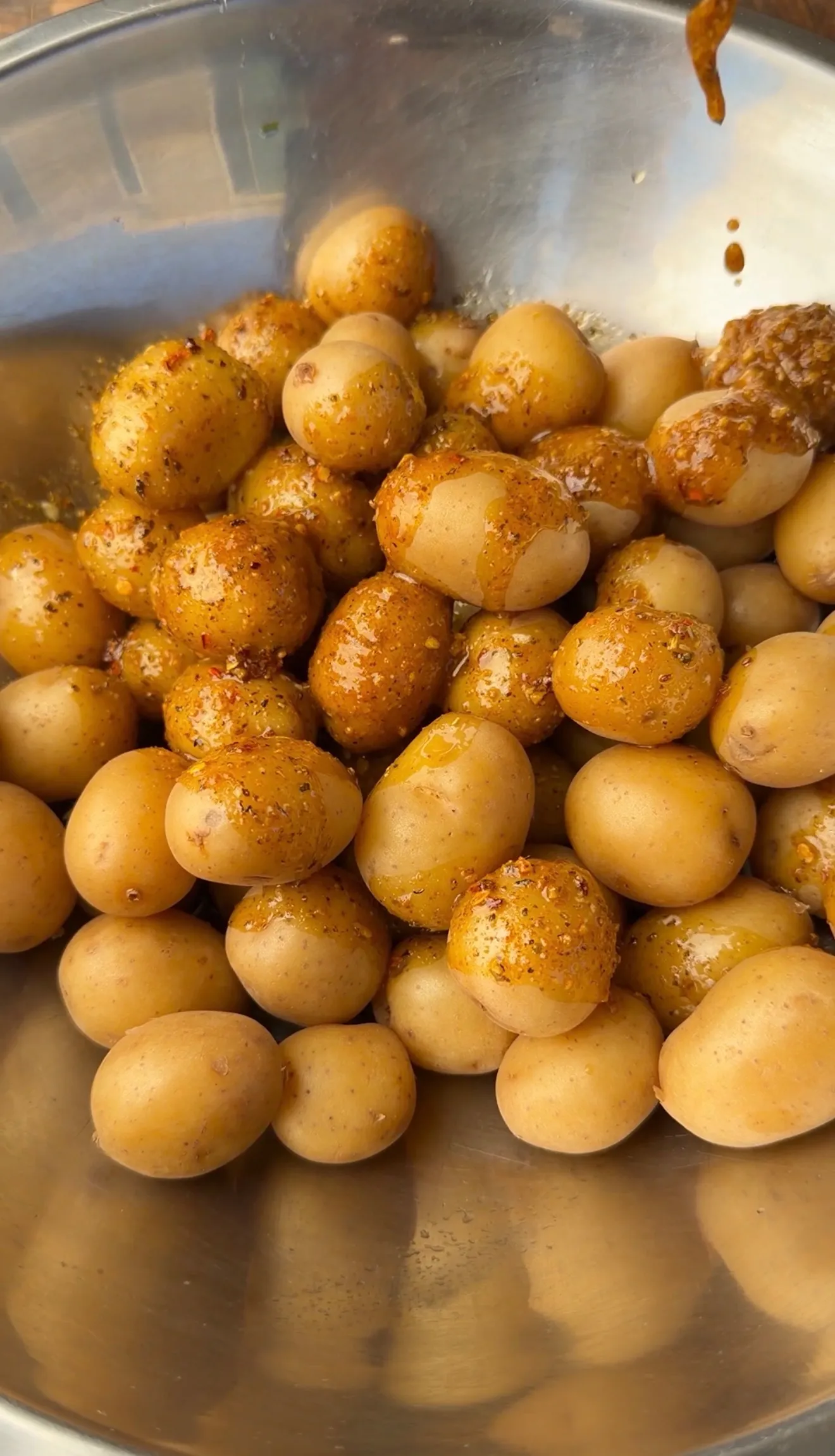 Golden seasoned mini potatoes with herbs and spices in a stainless steel mixing bowl ready for smashing