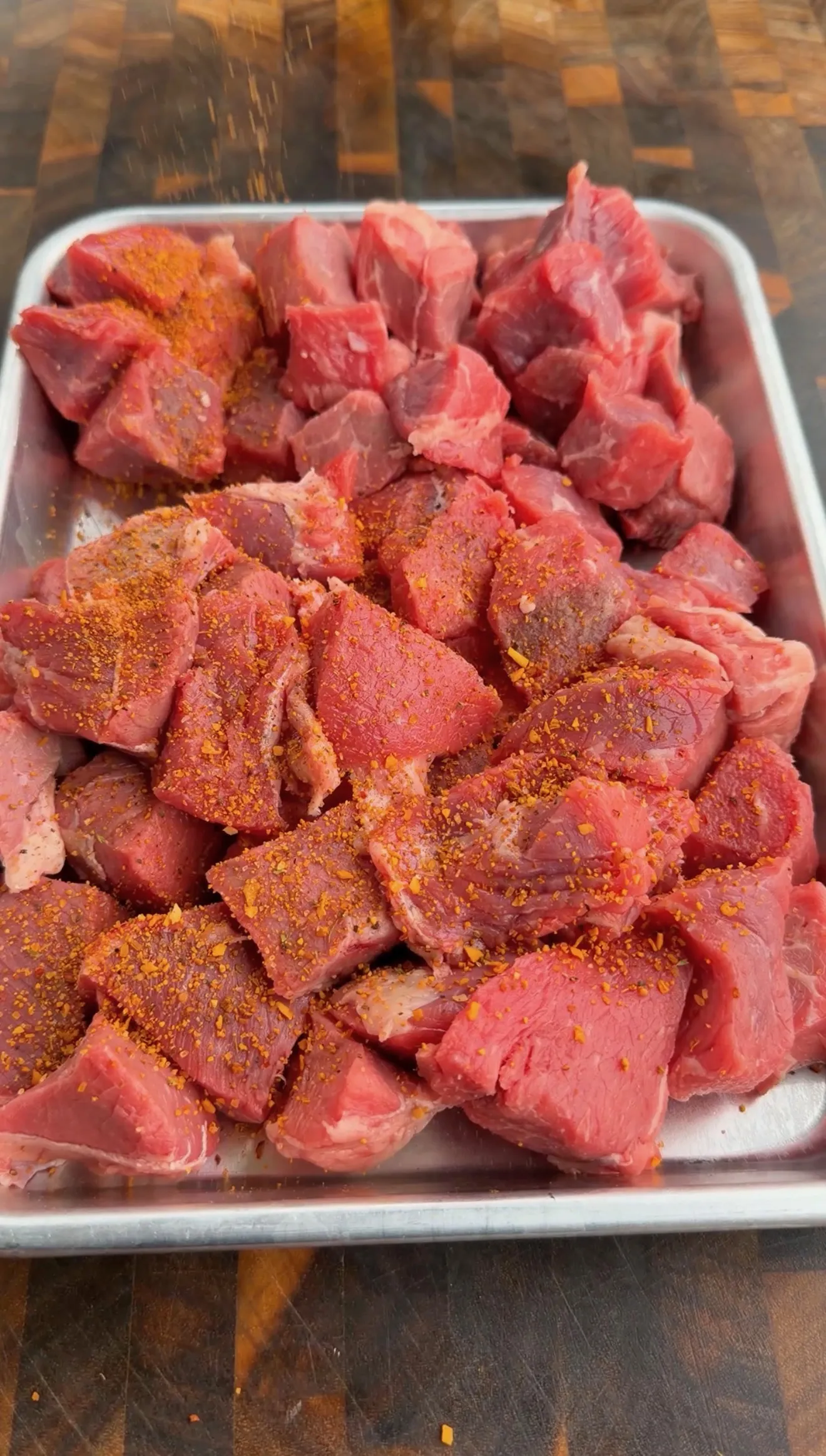 Raw beef chunks seasoned with spices in a white tray prepared for chimichurri steak kebabs