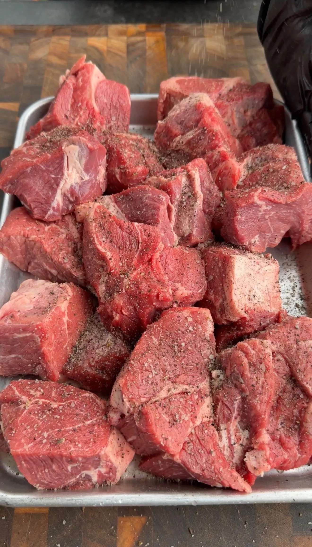 Raw beef chunks seasoned with spices in a metal baking pan, ready for slow cooking into pulled beef