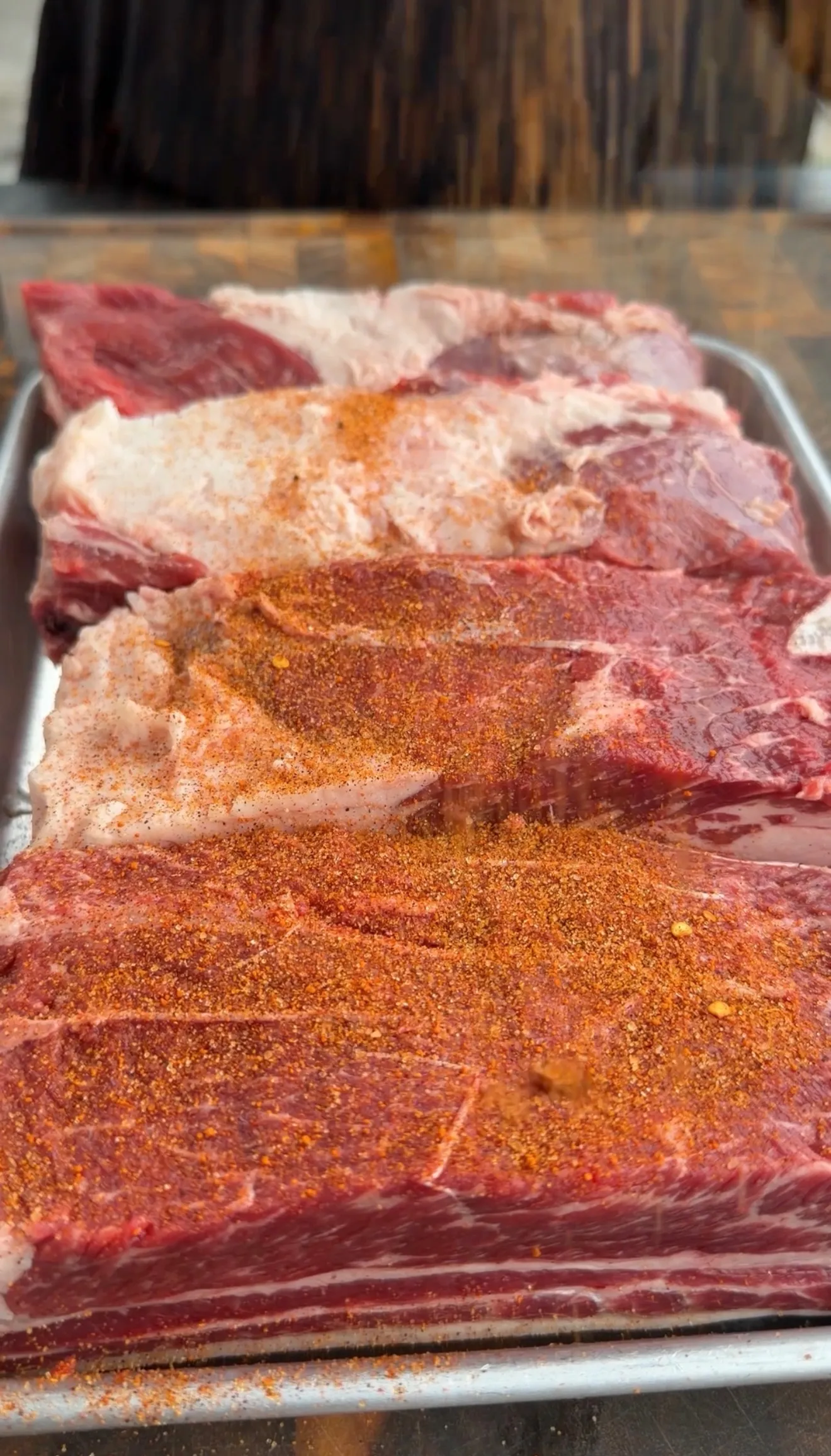 Raw beef ribs coated with barbecue spice rub on metal tray ready for smoking