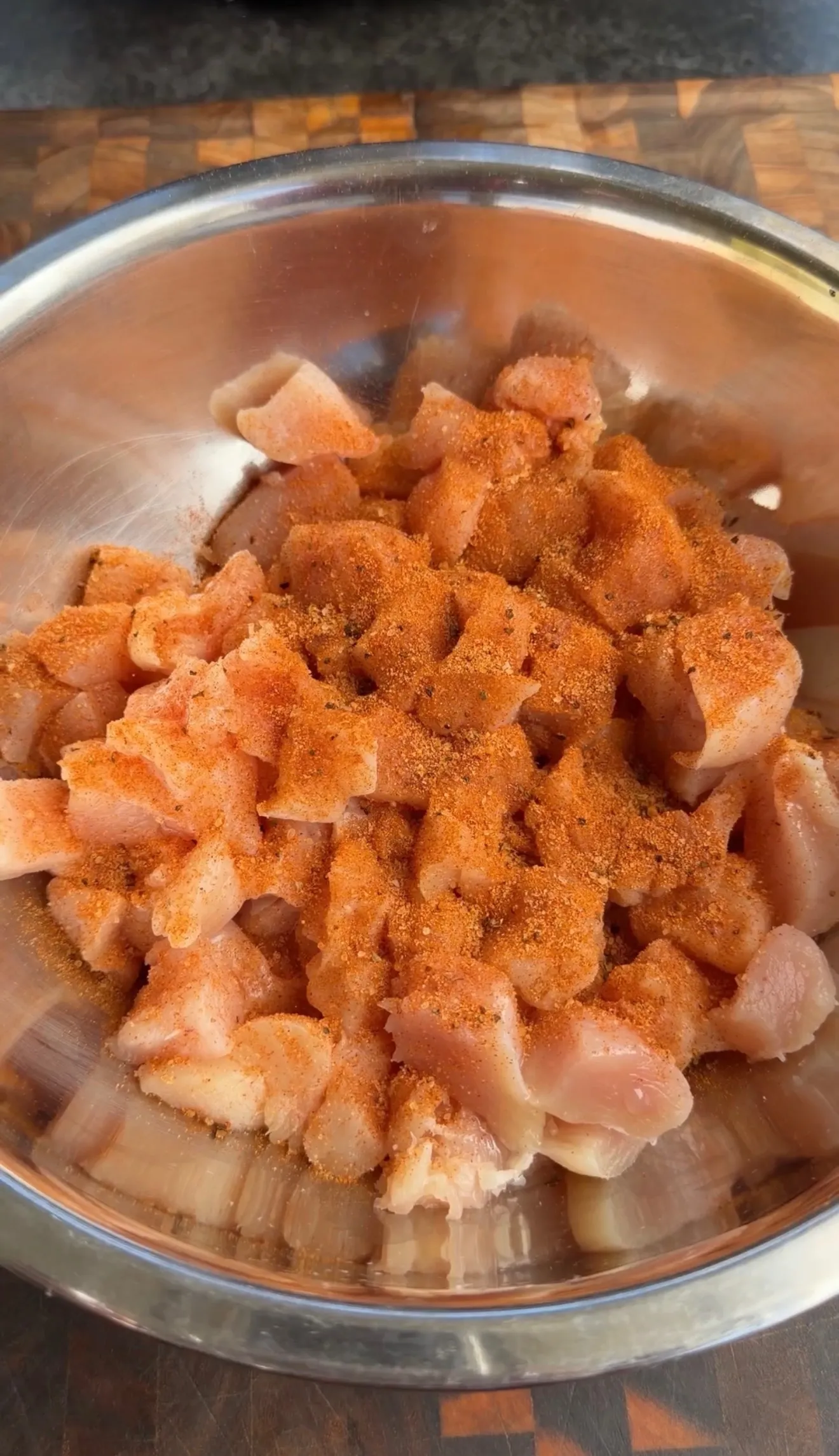 Seasoned raw chicken pieces in metal bowl