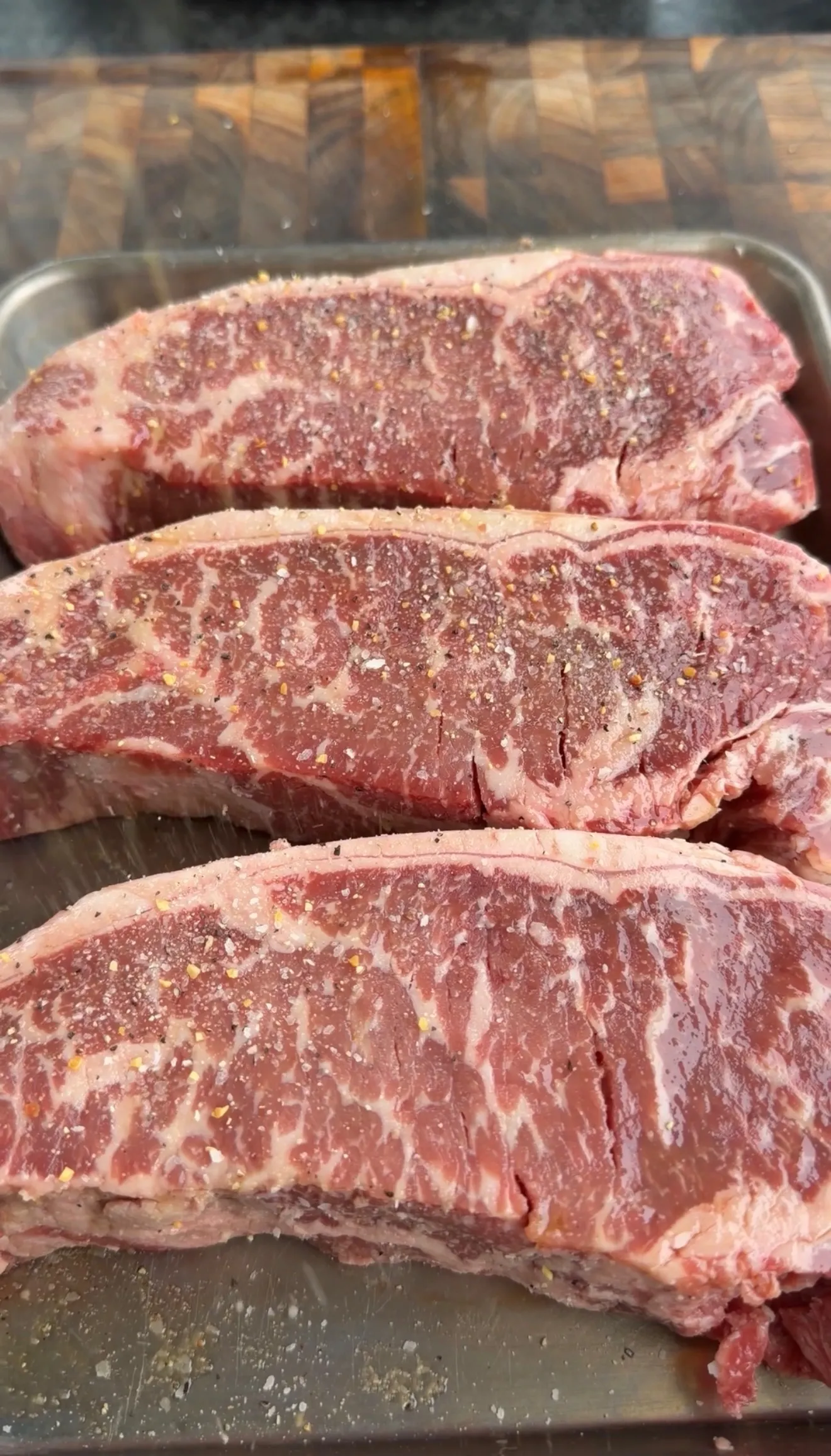 Seasoned raw strip steaks on metal tray