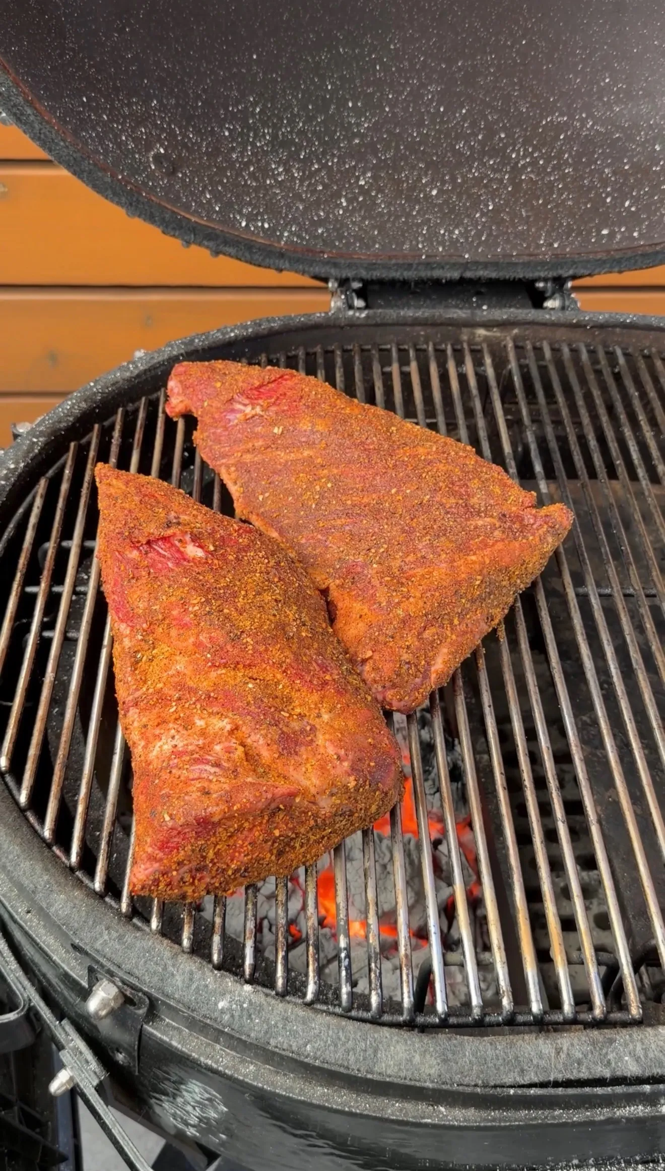 Three seasoned tri-tip roasts with spice rub cooking on a round charcoal grill with glowing coals