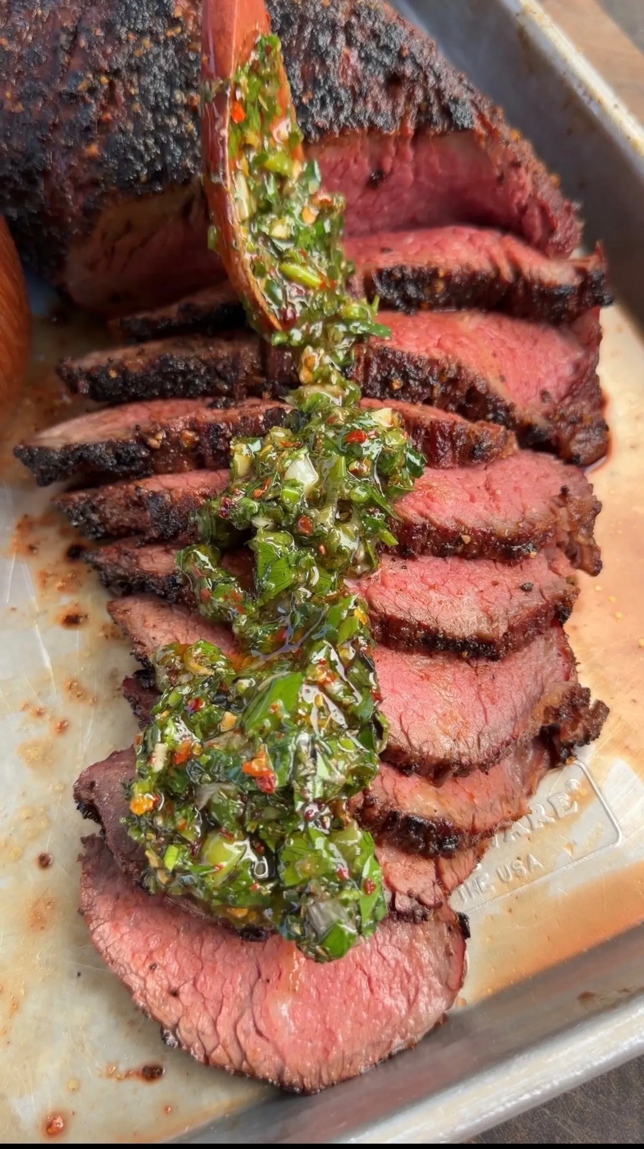 Sliced grilled tri-tip roast with charred crust topped with green onion chimichurri on cutting board