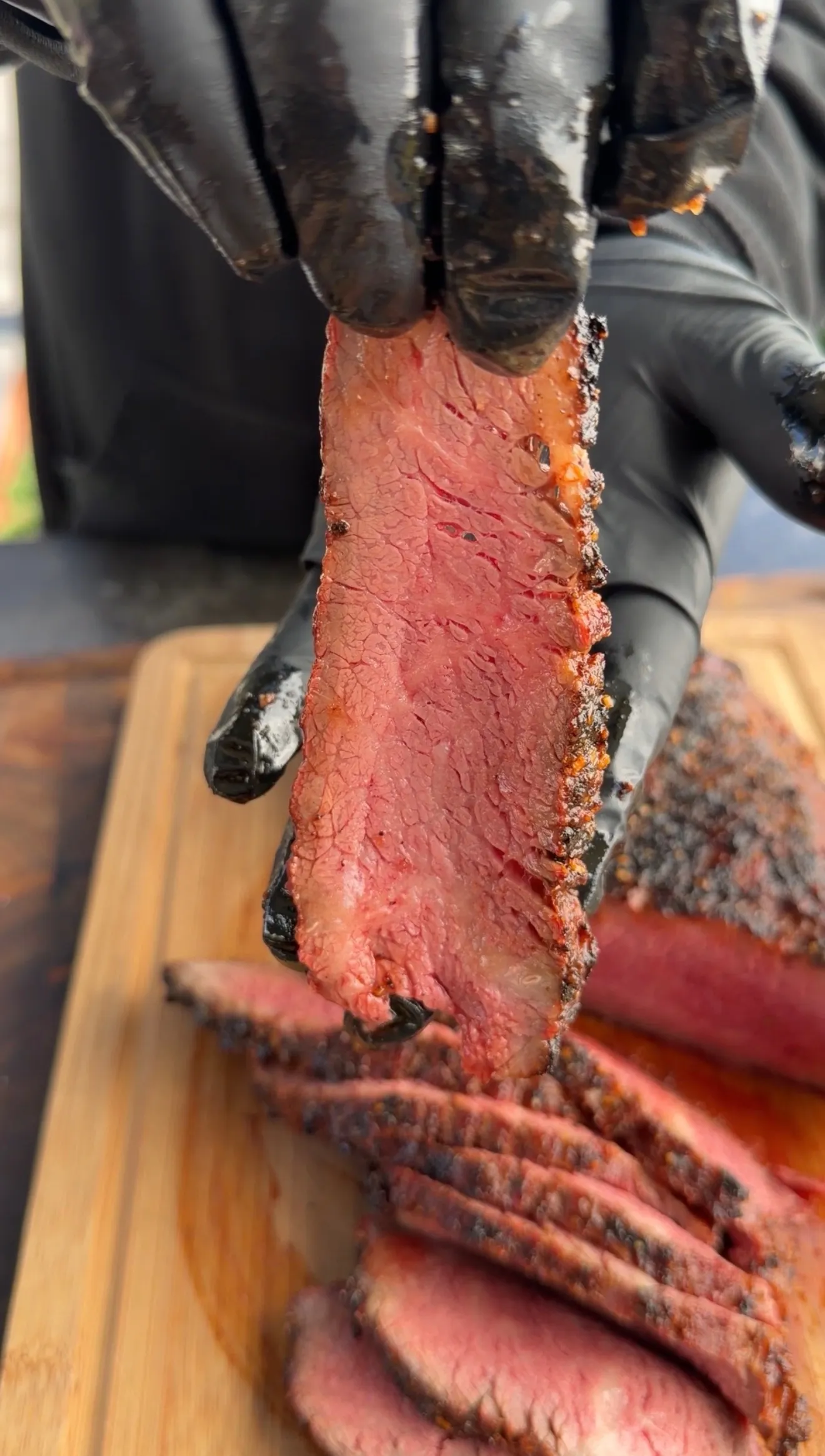 Hands holding a perfectly grilled medium-rare tri-tip roast slice showing pink interior and charred crust