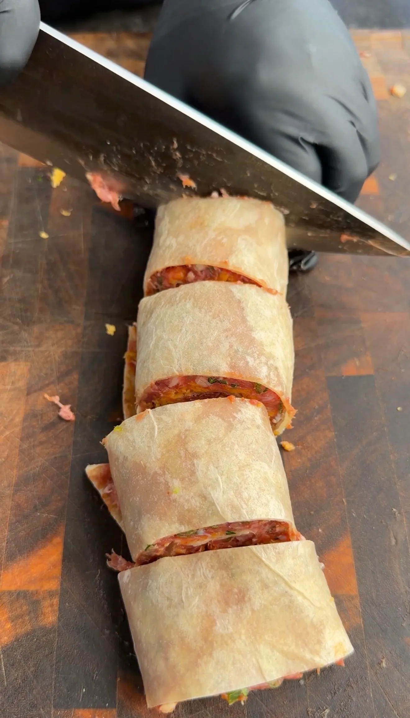 Grilled lamb tortilla pinwheel skewers sliced on wooden cutting board with chef's knife